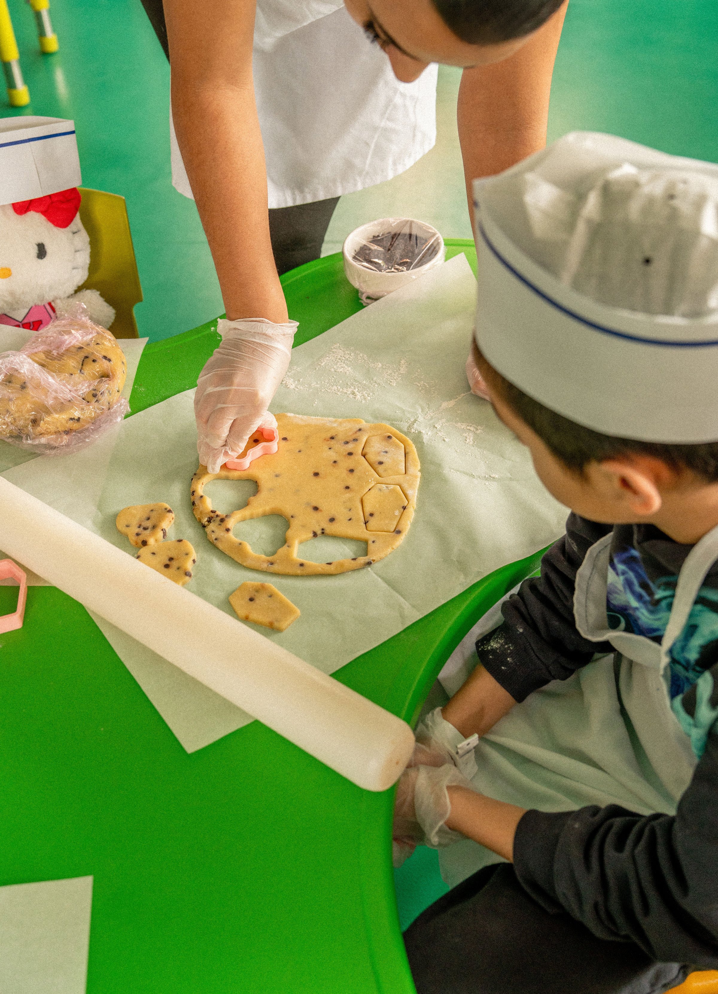 Kids' cooking class: adult and child baking chocolate chip cookies with cutters.