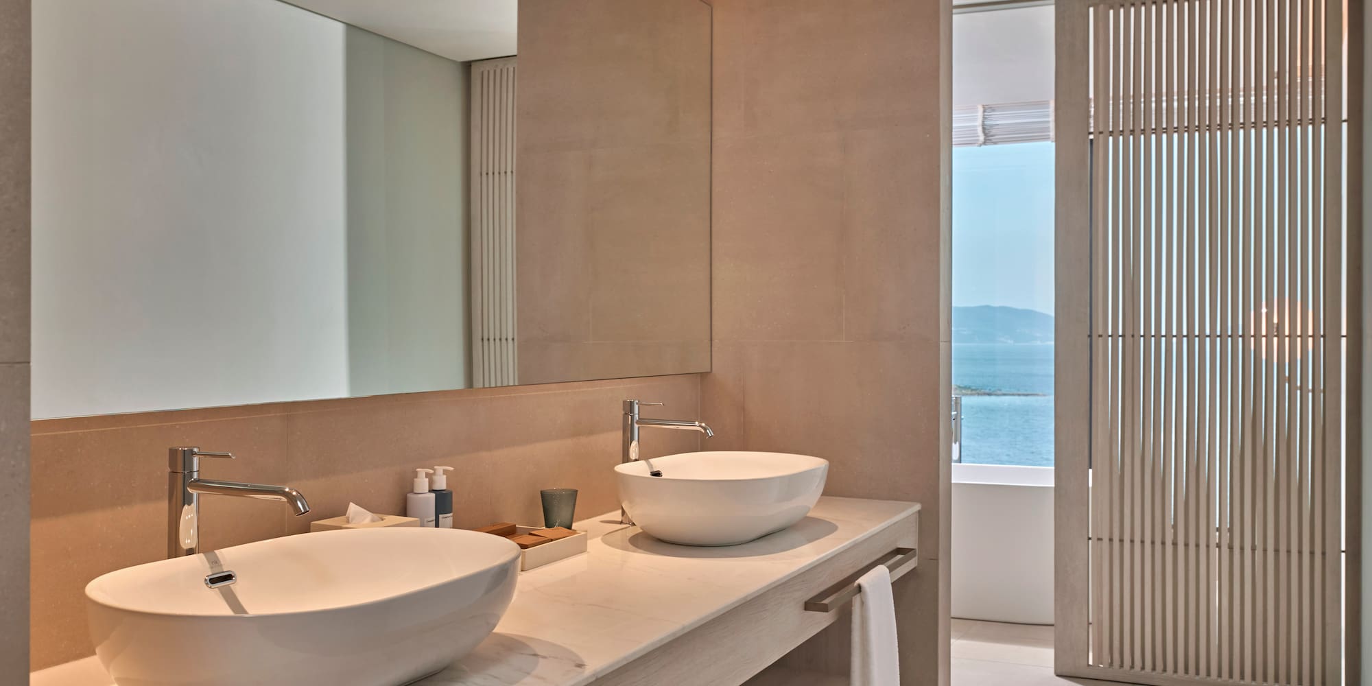Modern bathroom with double vessel sinks, marble vanity, and ocean view.