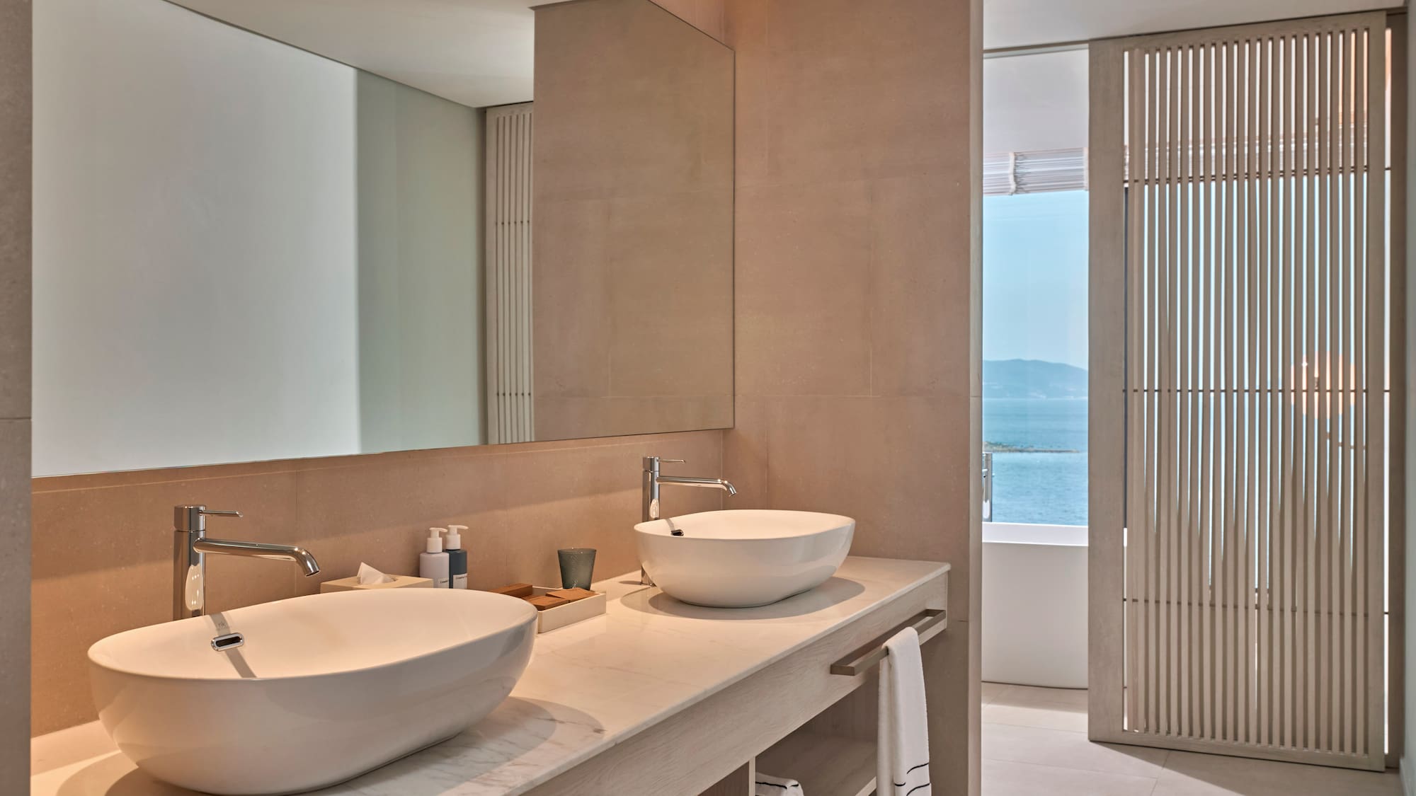 Modern bathroom with double vessel sinks, marble vanity, and ocean view.