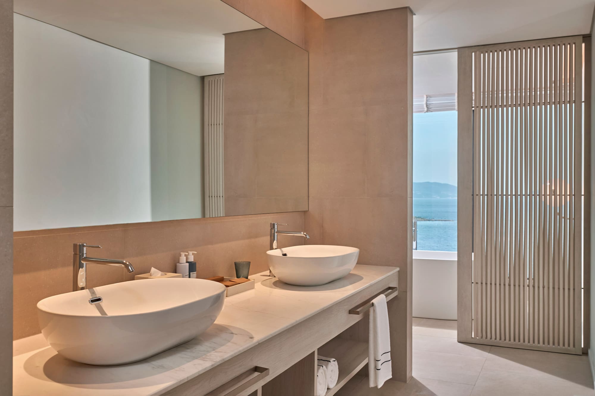 Modern bathroom with double vessel sinks, marble vanity, and ocean view.
