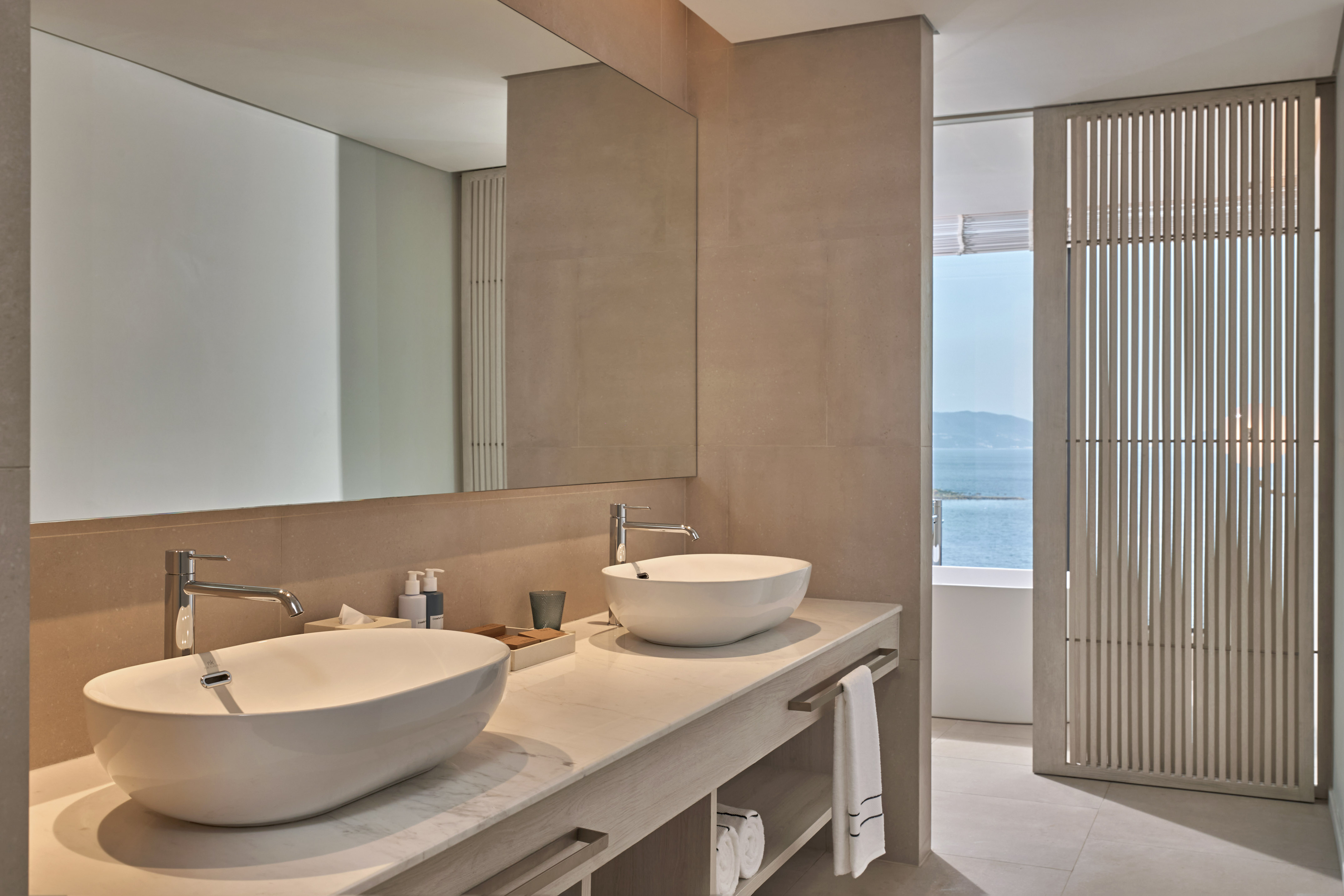 Modern bathroom with double vessel sinks, marble vanity, and ocean view.