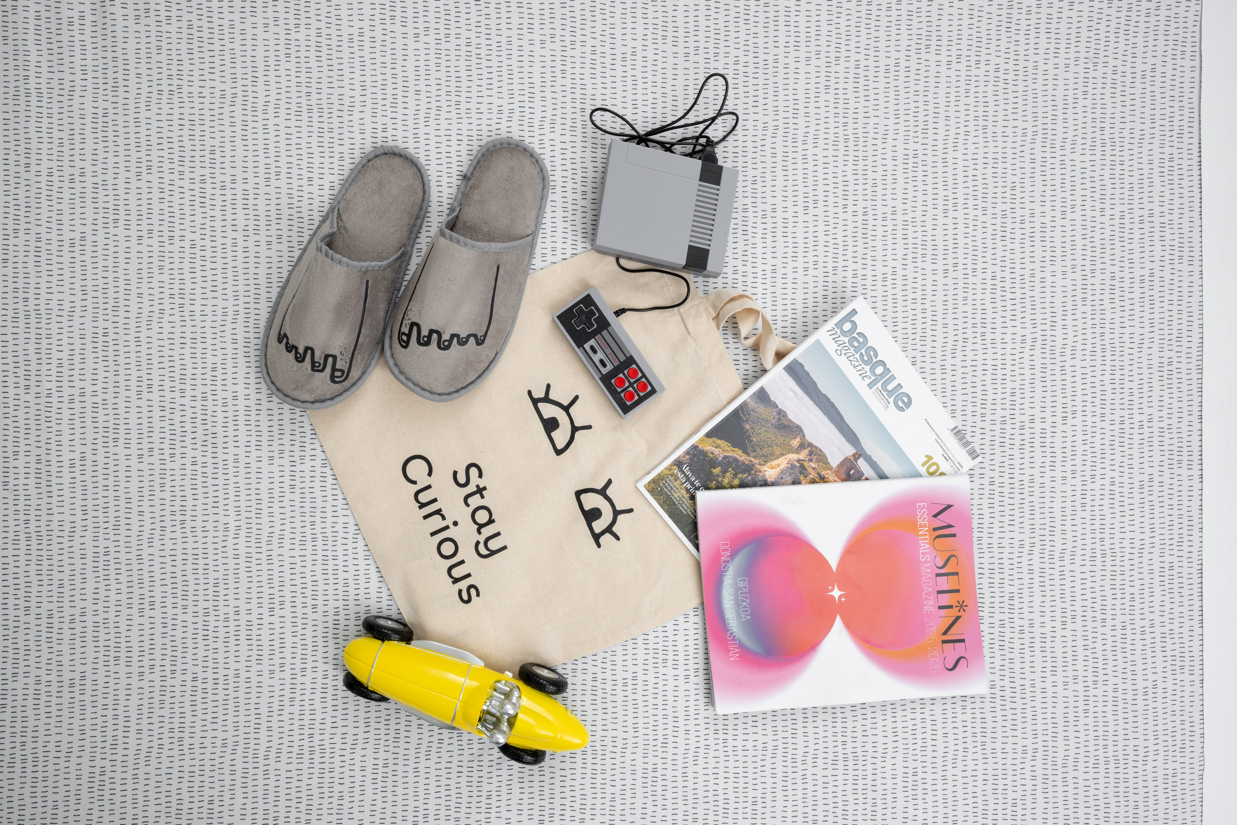 Ocio en casa: zapatillas, consola retro, revistas, coche juguete y bolsa.