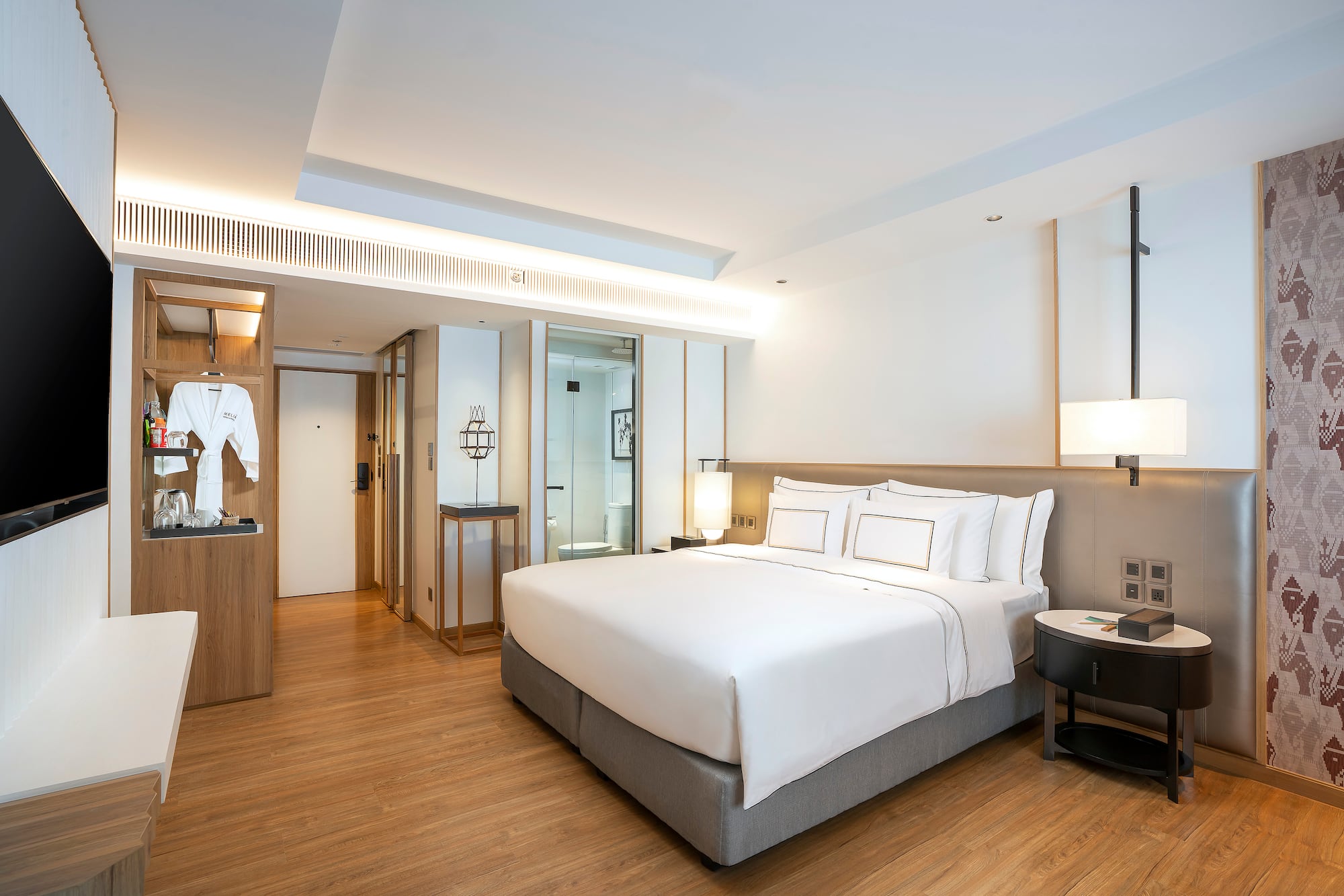 Modern hotel room with king bed, wood floor, and open minibar area.