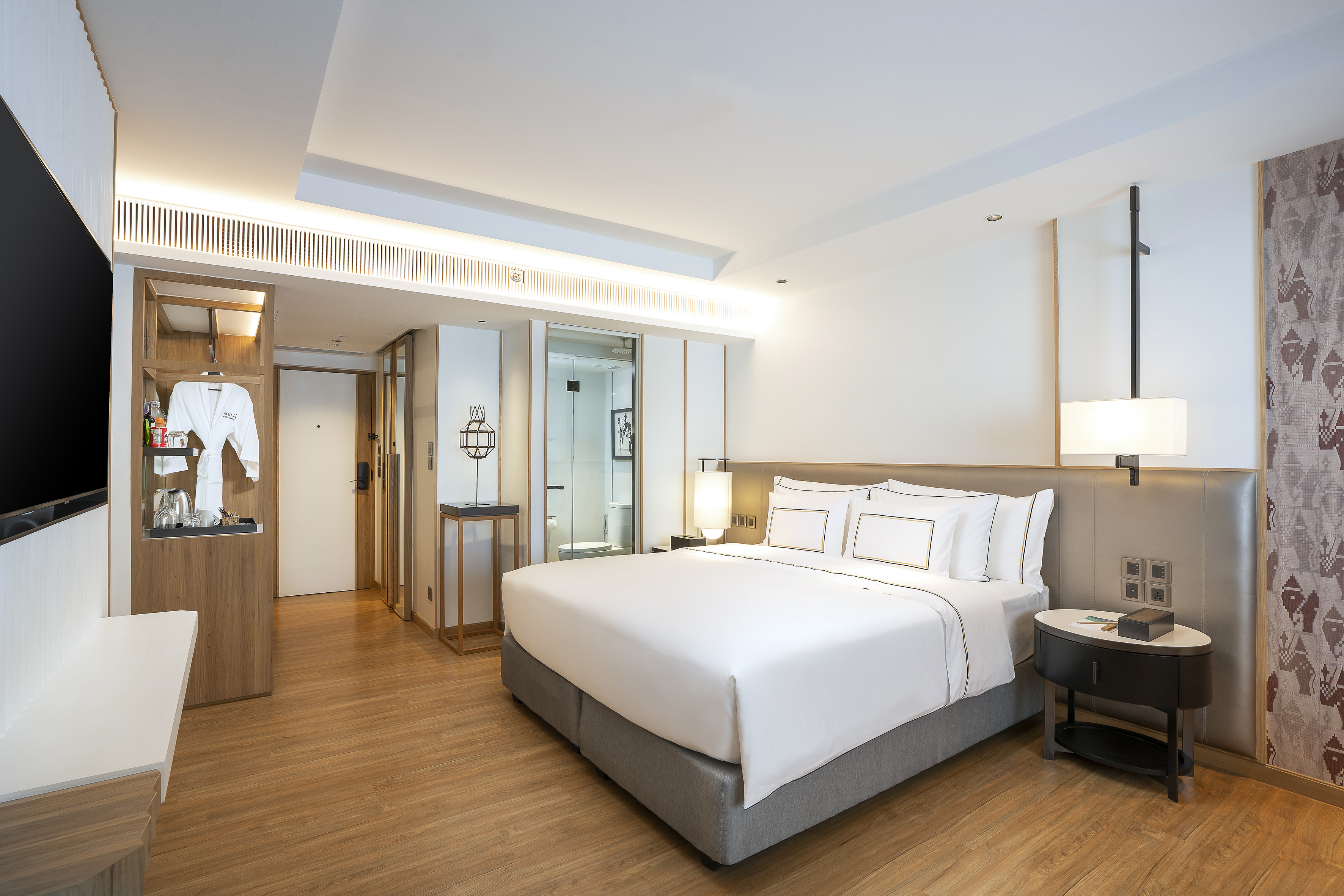 Modern hotel room with king bed, wood floor, and open minibar area.