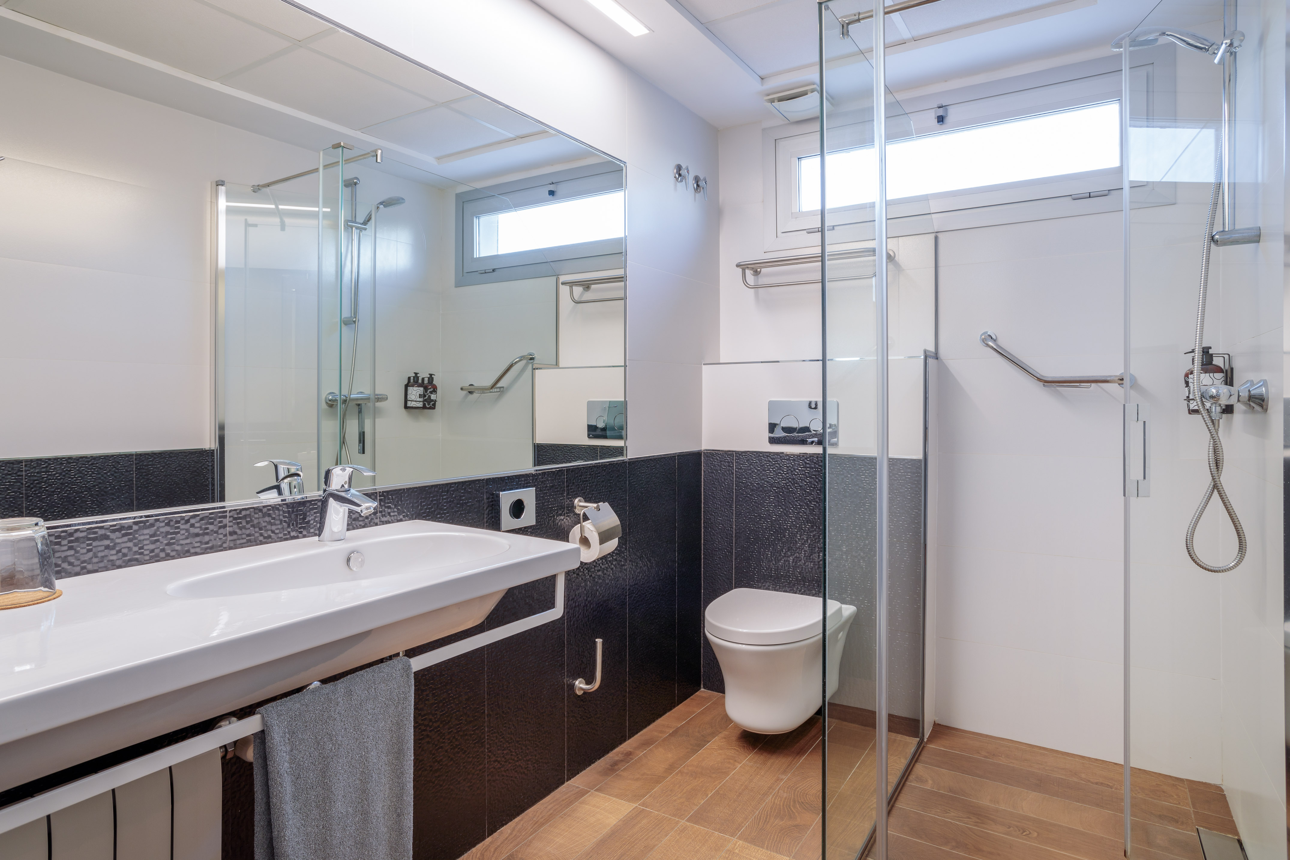 Accessible modern bathroom with sink, toilet, glass shower, and grab bars.