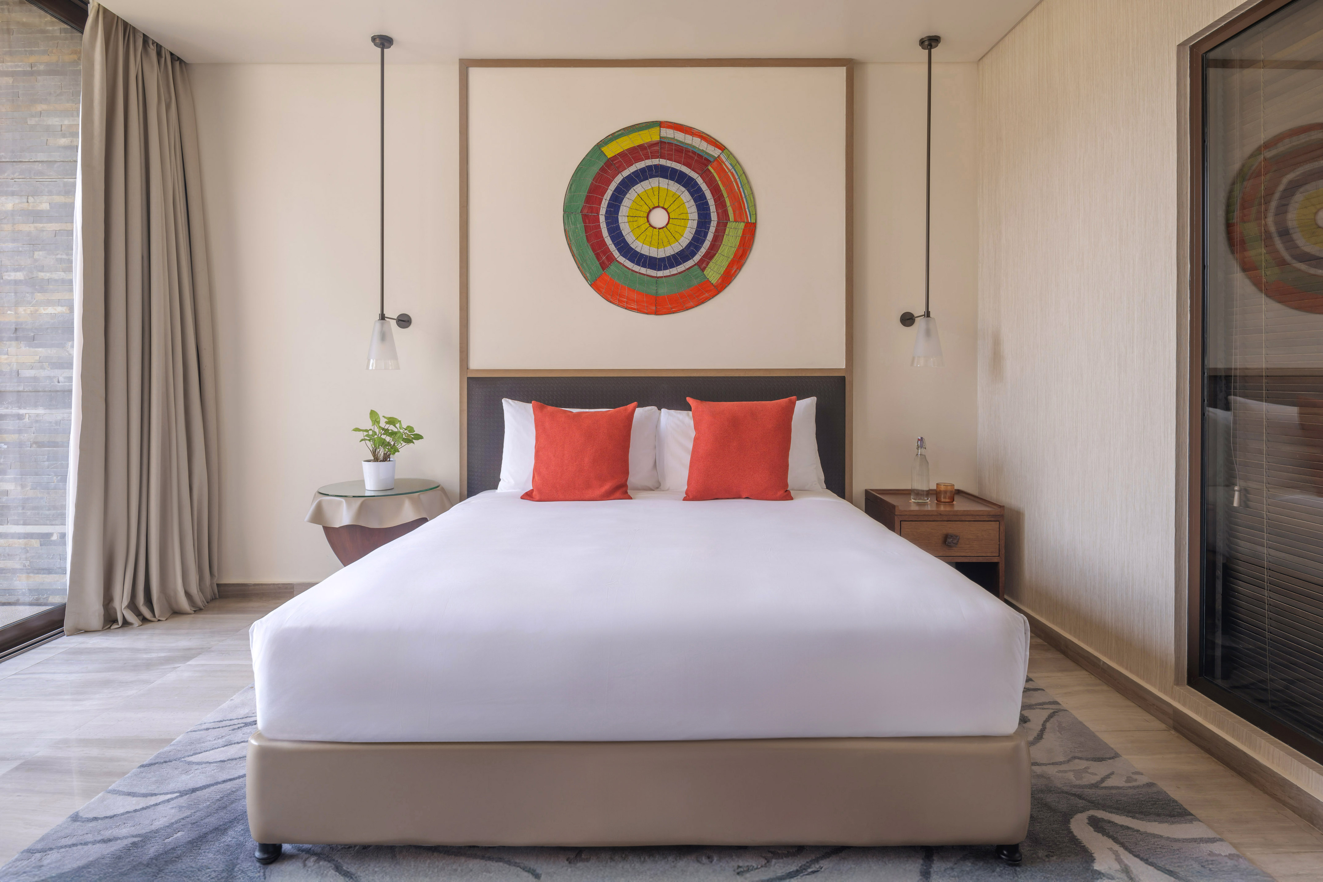 Bright hotel bedroom, king bed with orange pillows, abstract wall art.