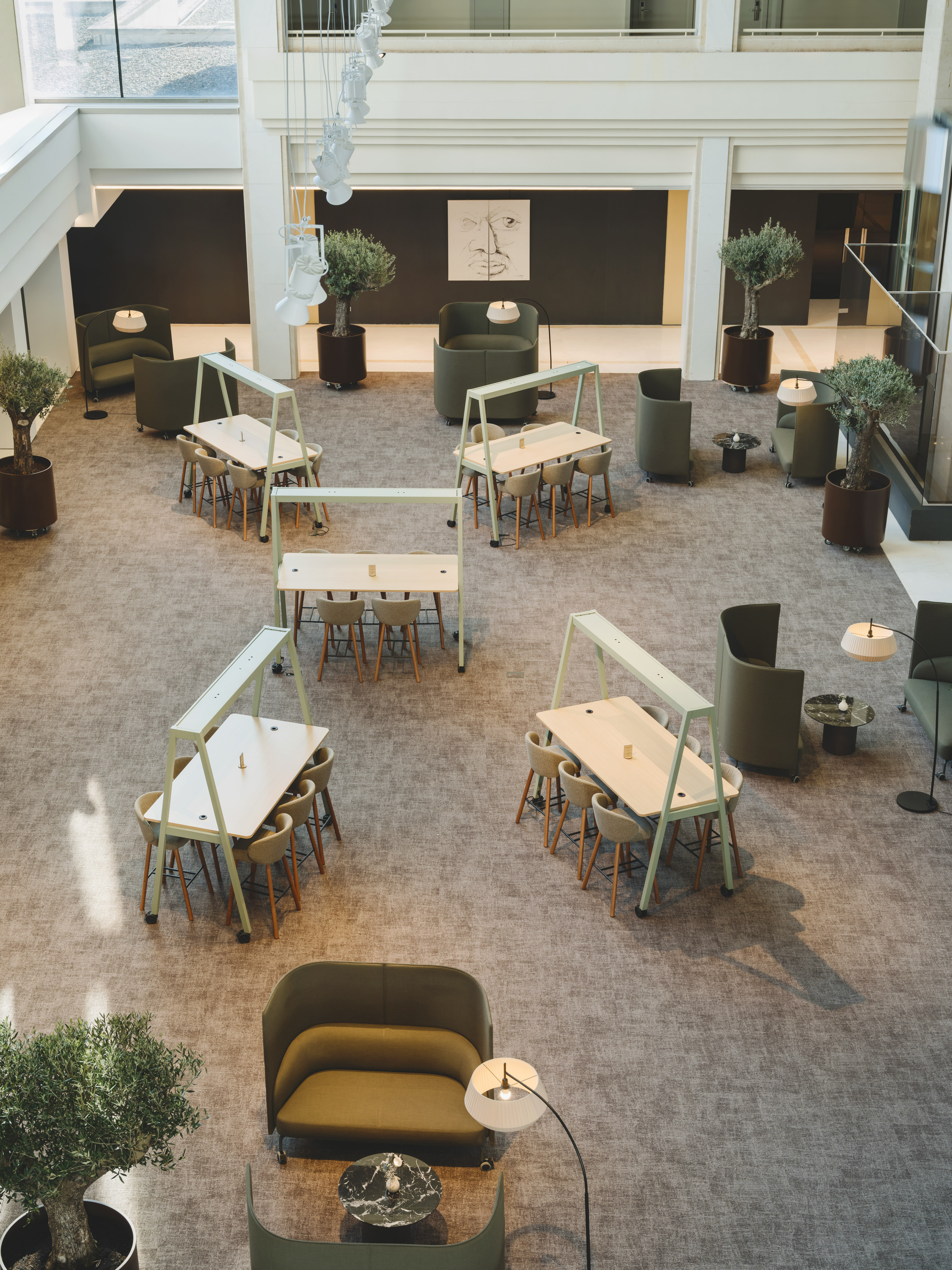 Modern office lobby with green lounge chairs, collaborative tables, and olive trees.