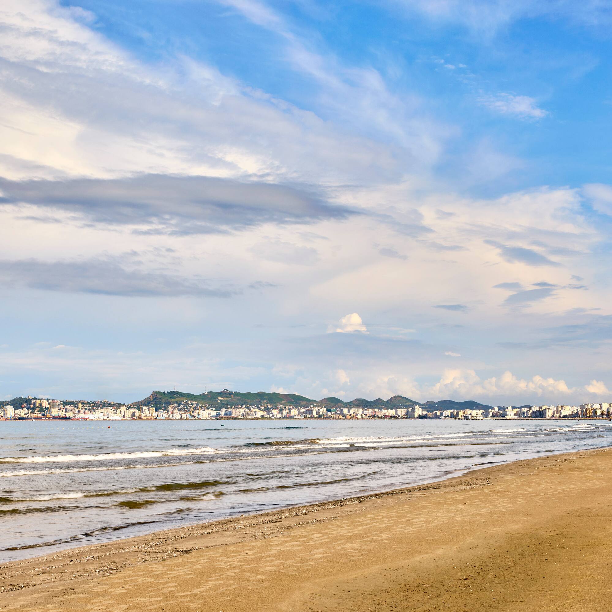 a beach with a body of water and buildings in the background