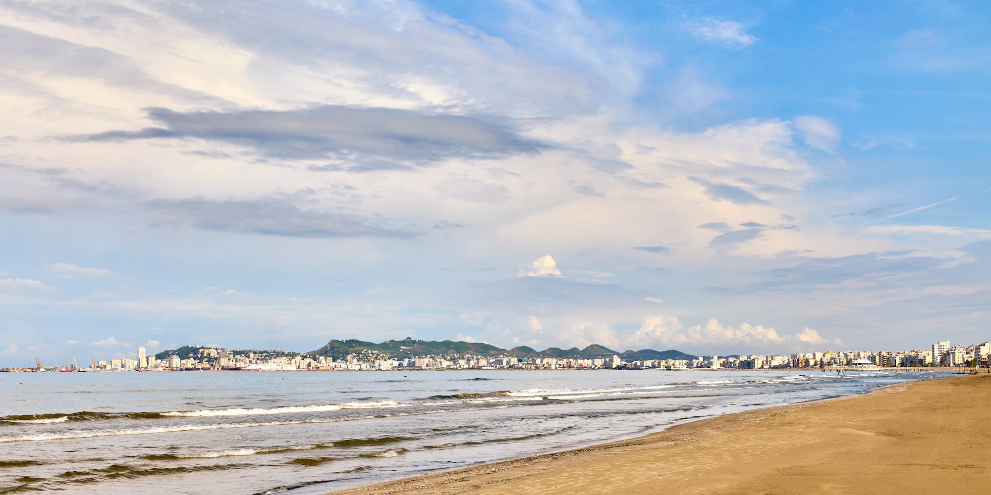 a beach with a body of water and buildings in the background