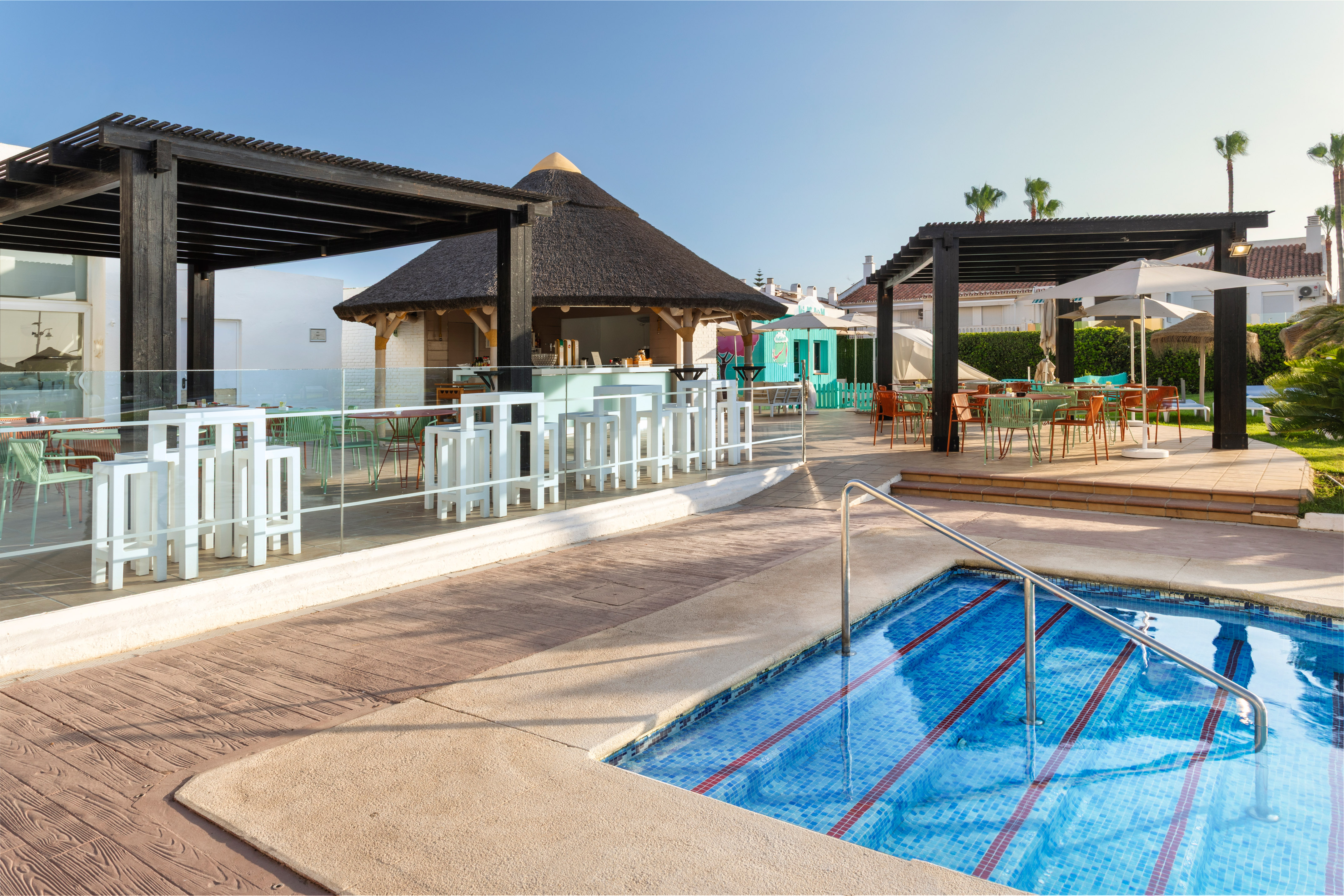 Sunny resort pool with thatched bar and shaded outdoor dining areas.