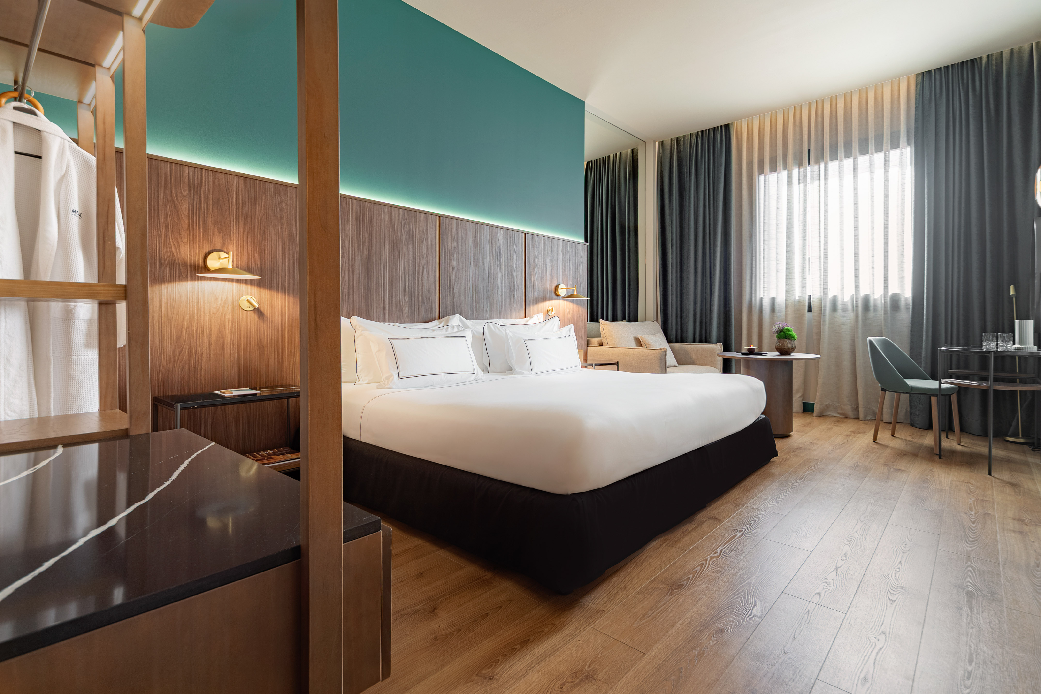Luxury hotel room with king bed, teal wall, wood details, and desk.