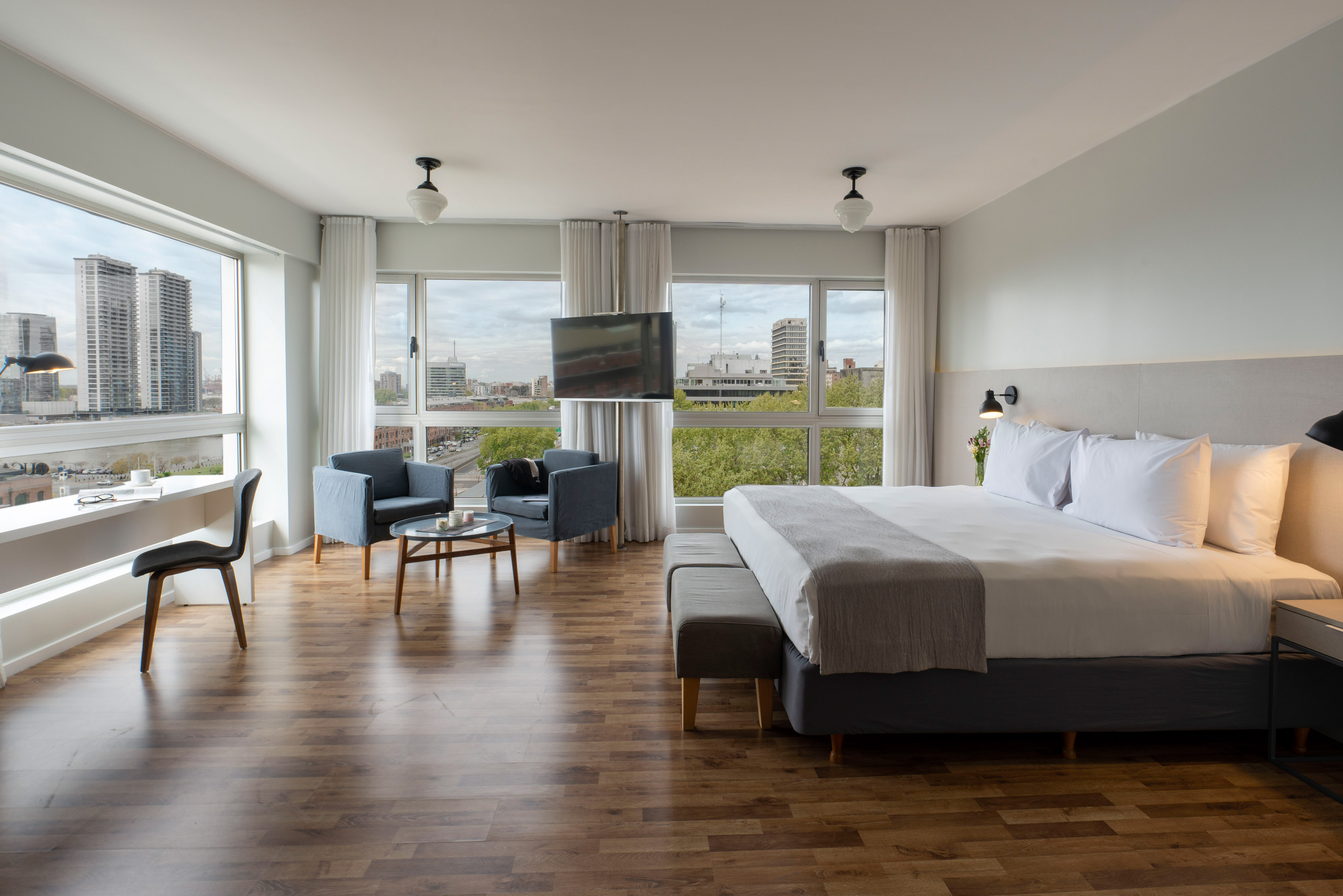 Modern hotel suite with city views, large bed, desk, and lounge area.