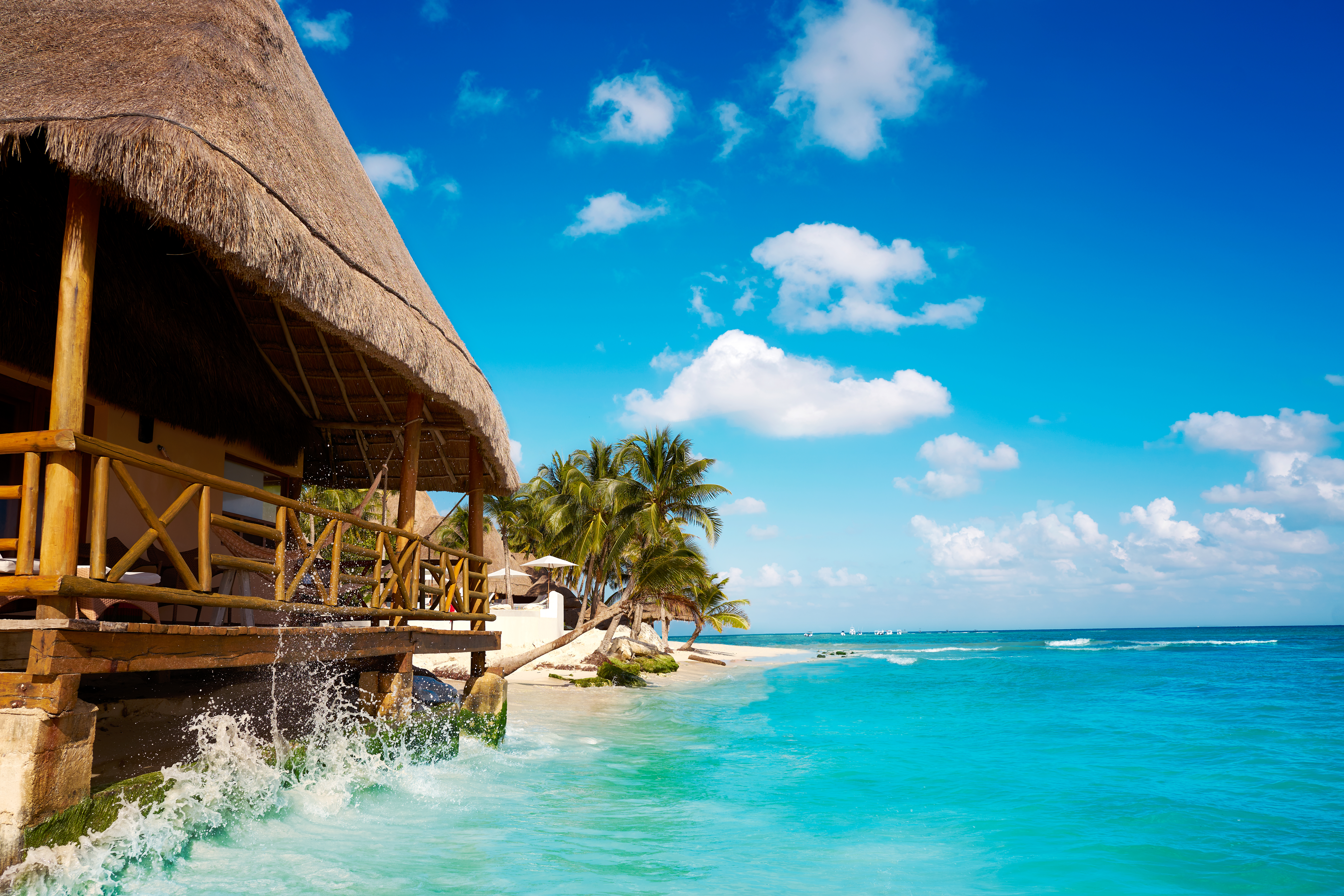 Cabaña con techo de paja sobre agua turquesa, playa tropical caribeña.