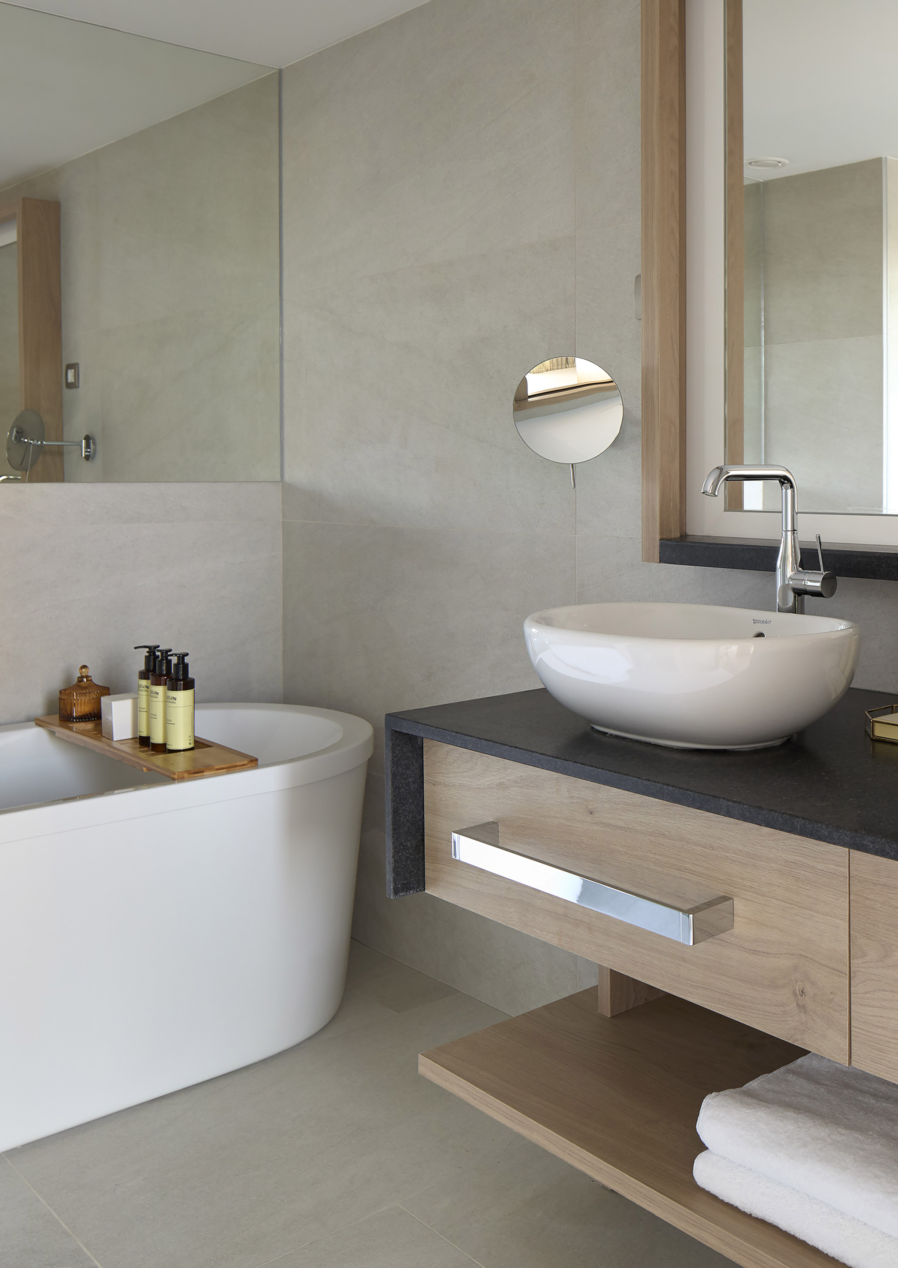Modern bathroom with white bathtub, wooden caddy, vanity, and vessel sink.