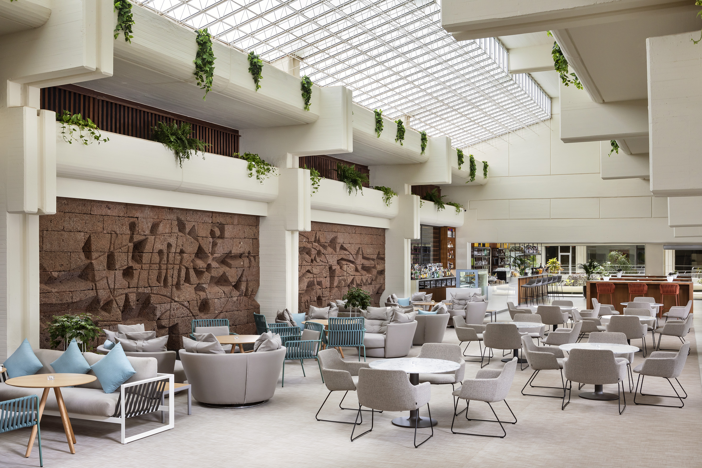 Modern hotel lounge with skylight, comfortable seating, and indoor plants.