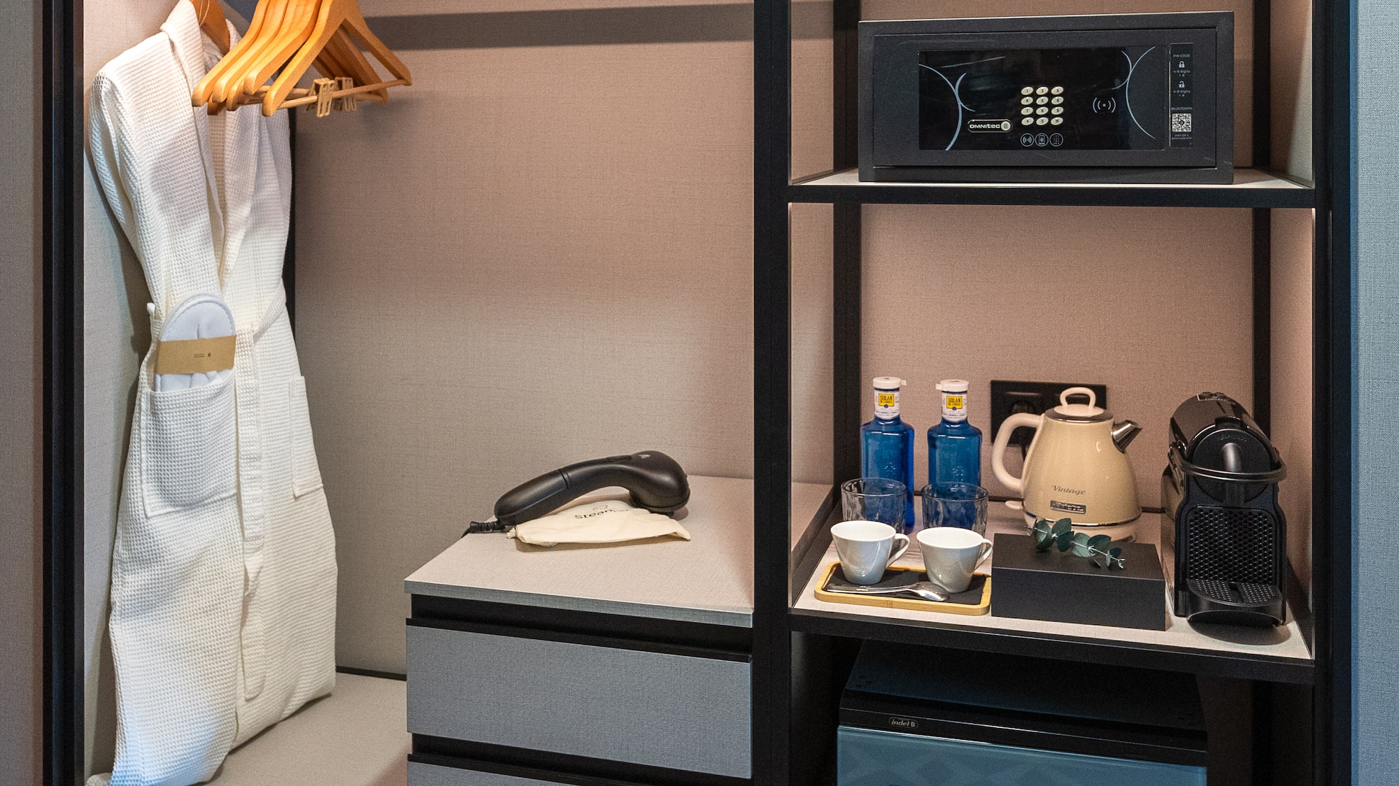 Modern hotel wardrobe with bathrobe, safe, minibar, Nespresso machine, and kettle.