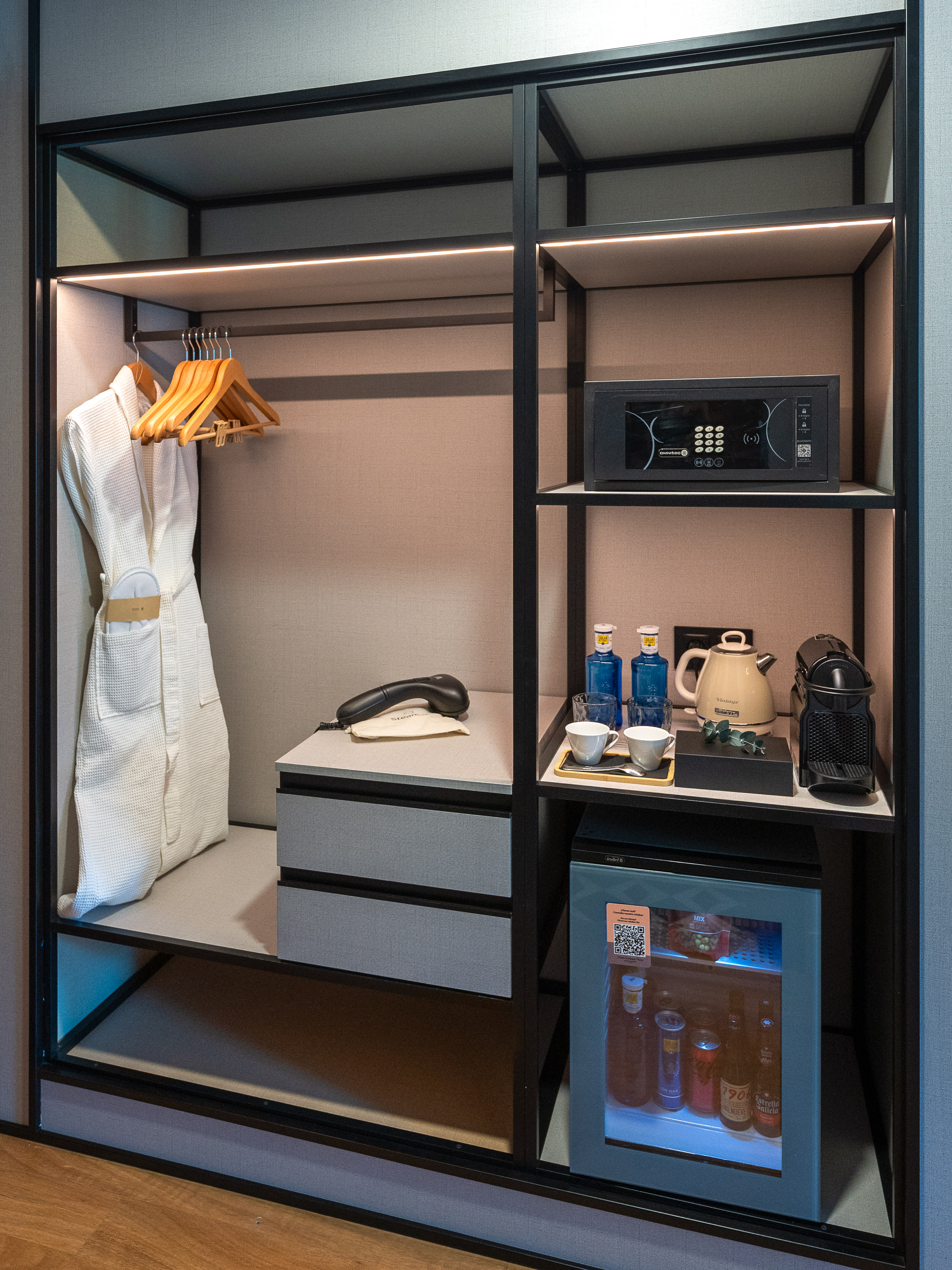 Modern hotel wardrobe with bathrobe, safe, minibar, Nespresso machine, and kettle.