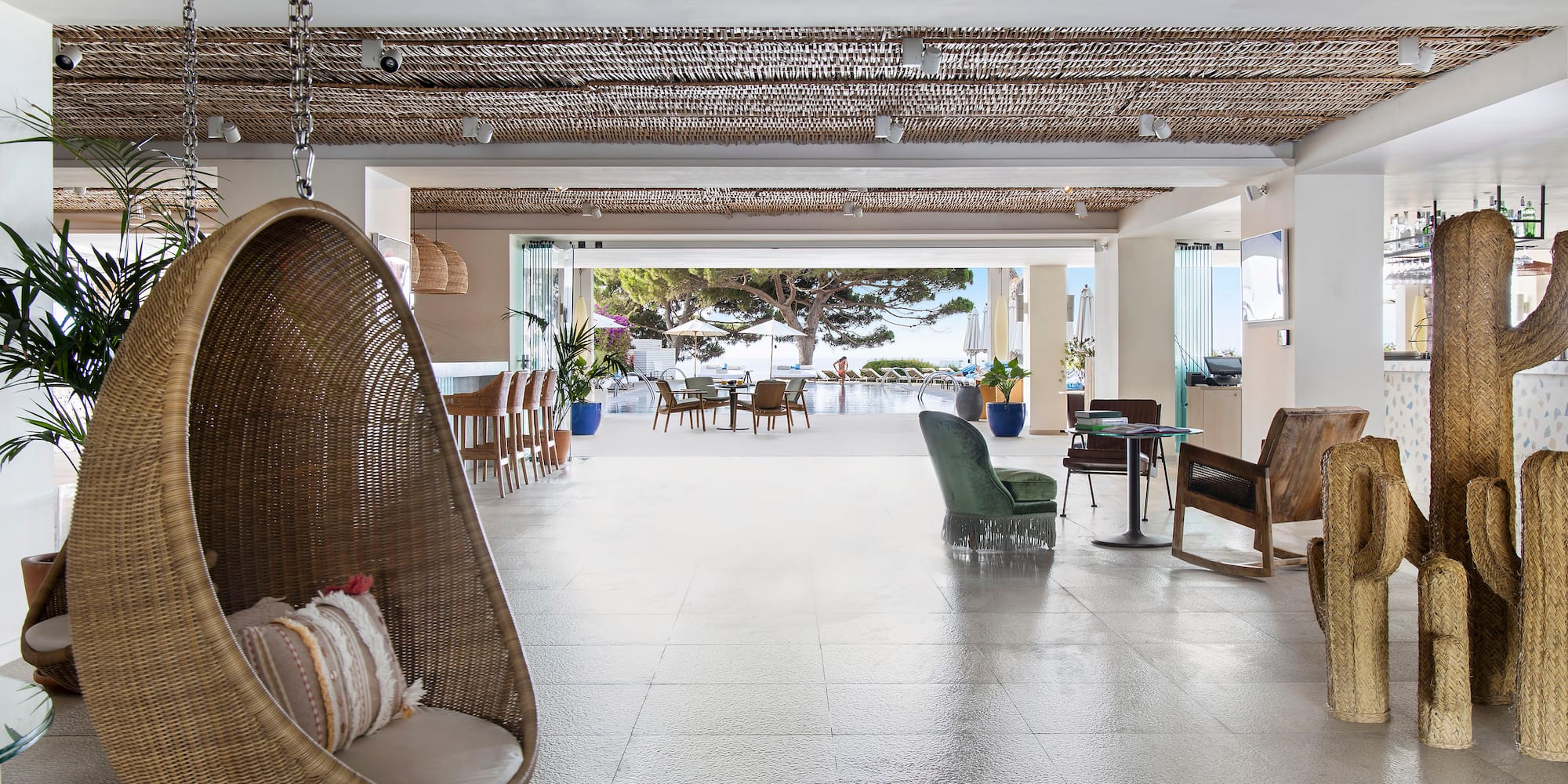 Wicker hanging chair in resort lobby with open pool view to ocean.