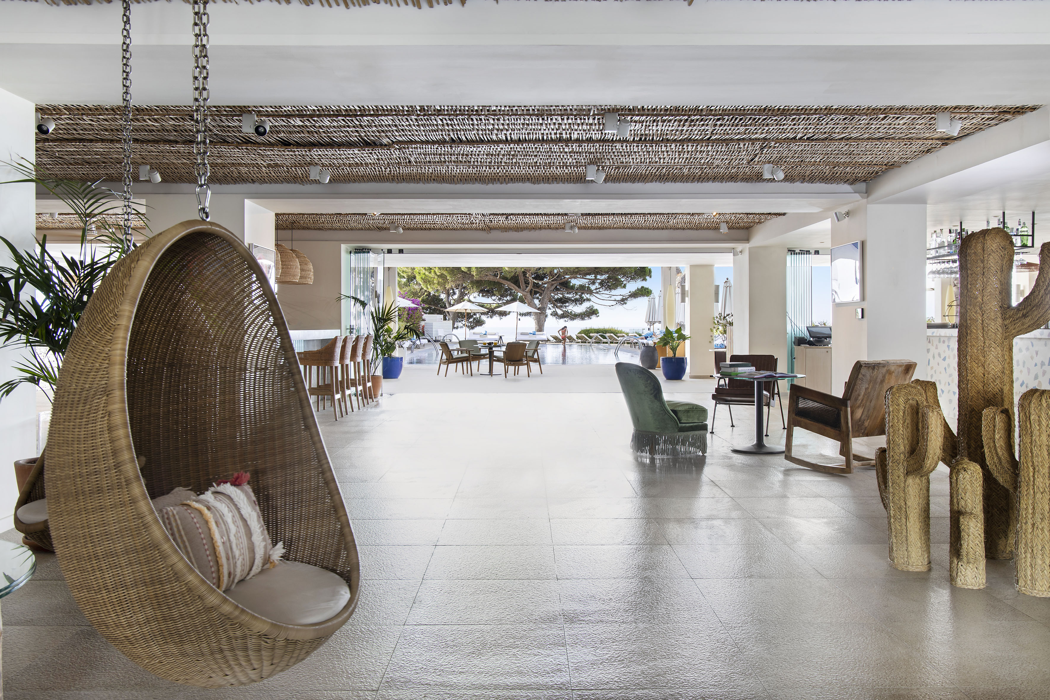 Wicker hanging chair in resort lobby with open pool view to ocean.