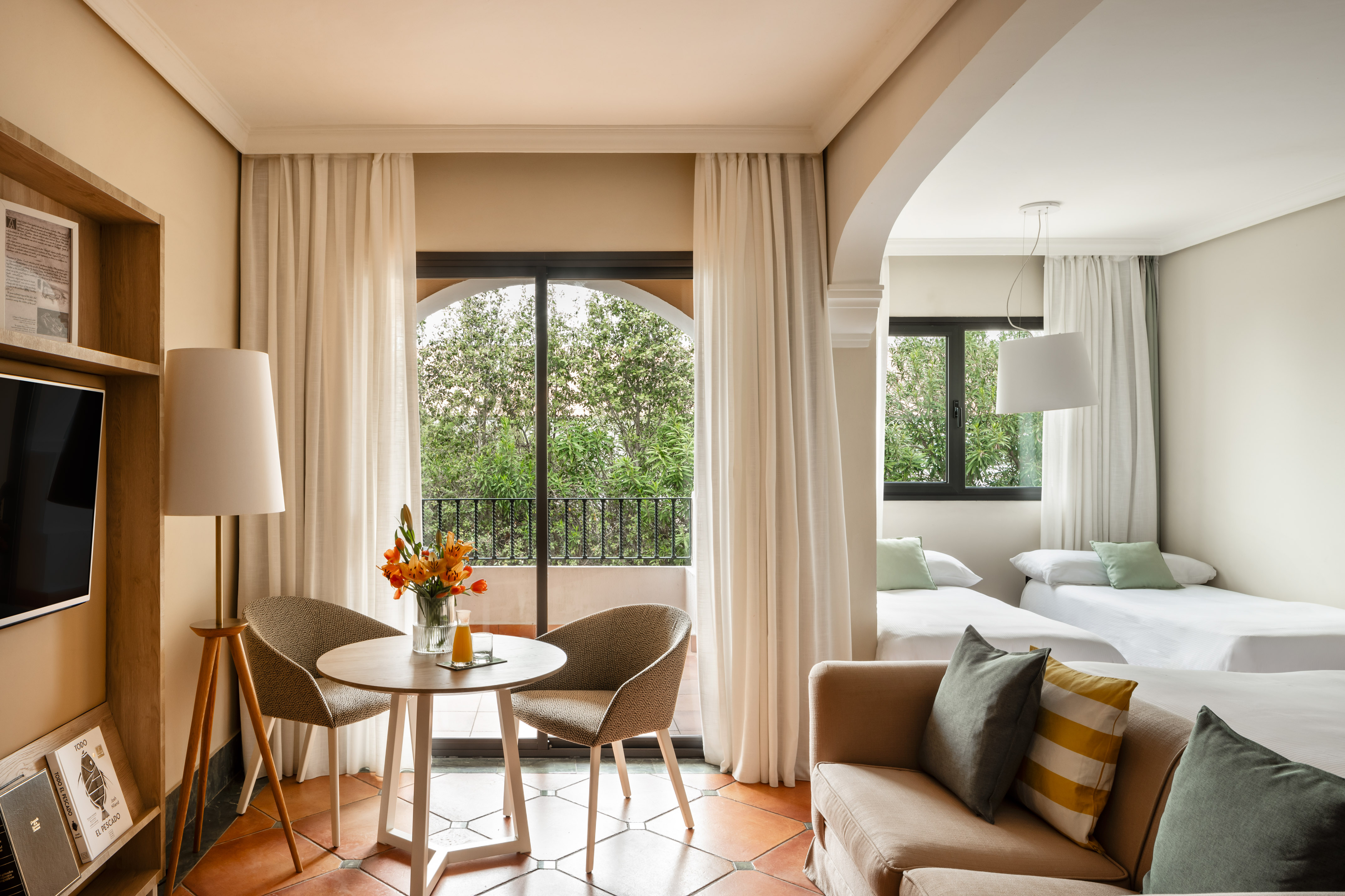 Mediterranean-style hotel suite with living area, balcony, and twin beds.
