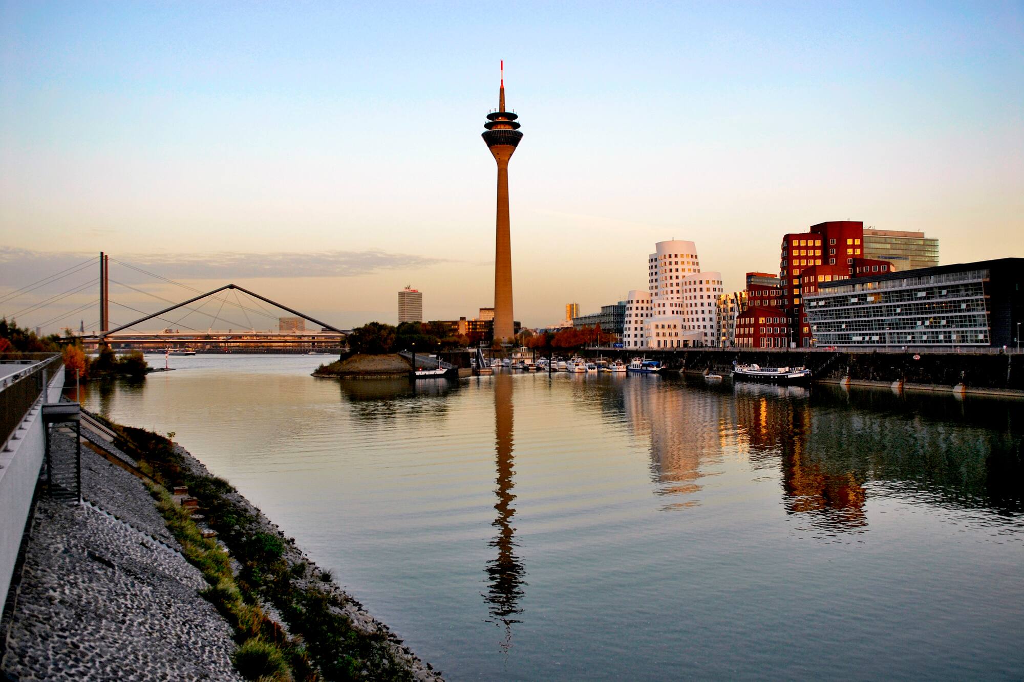 Düsseldorf Rheinturm, MedienHafen, and Rhine river at sunset with reflections.