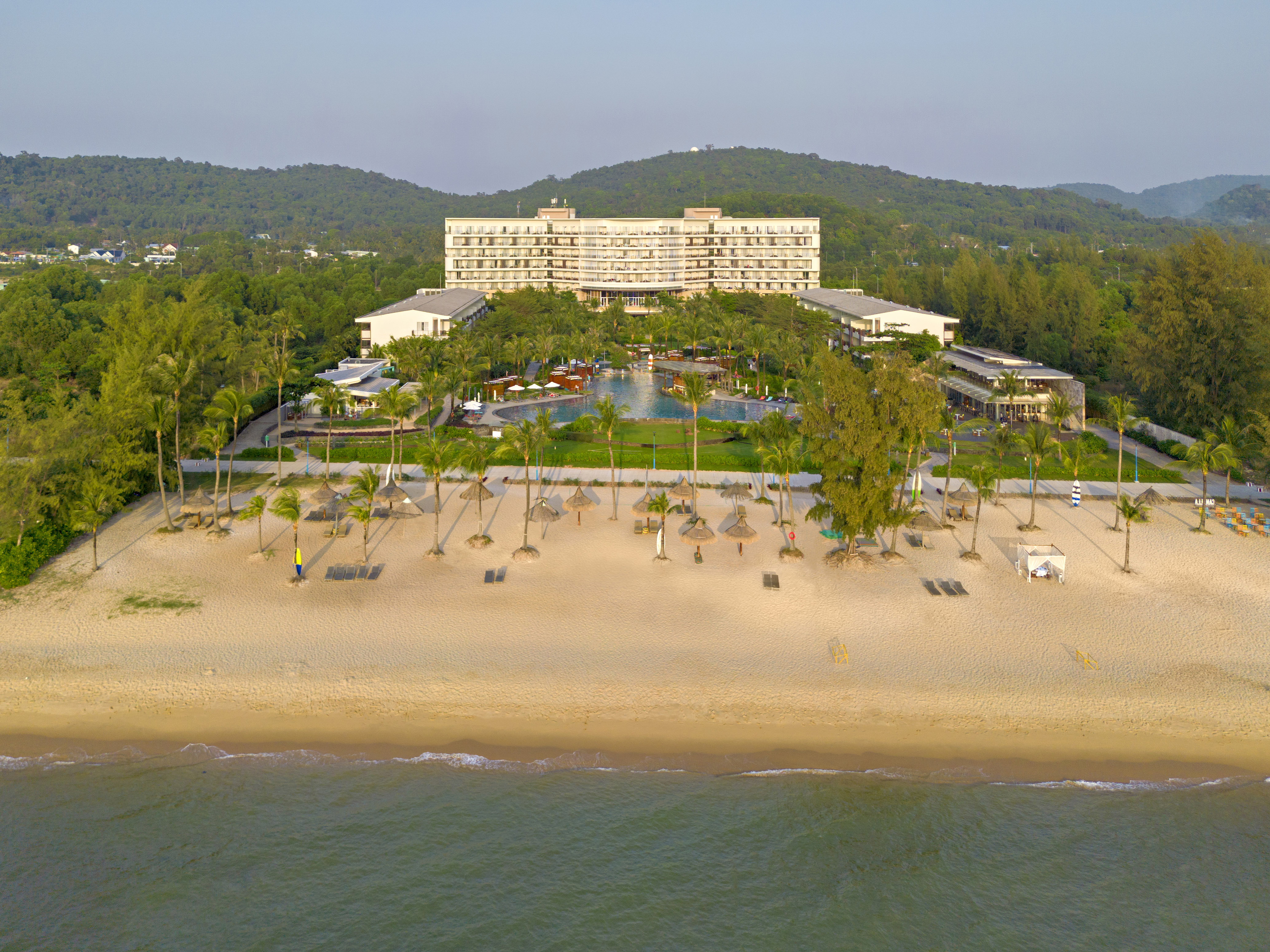 Tropical resort on sandy beach with large hotel, pools, and palm trees.