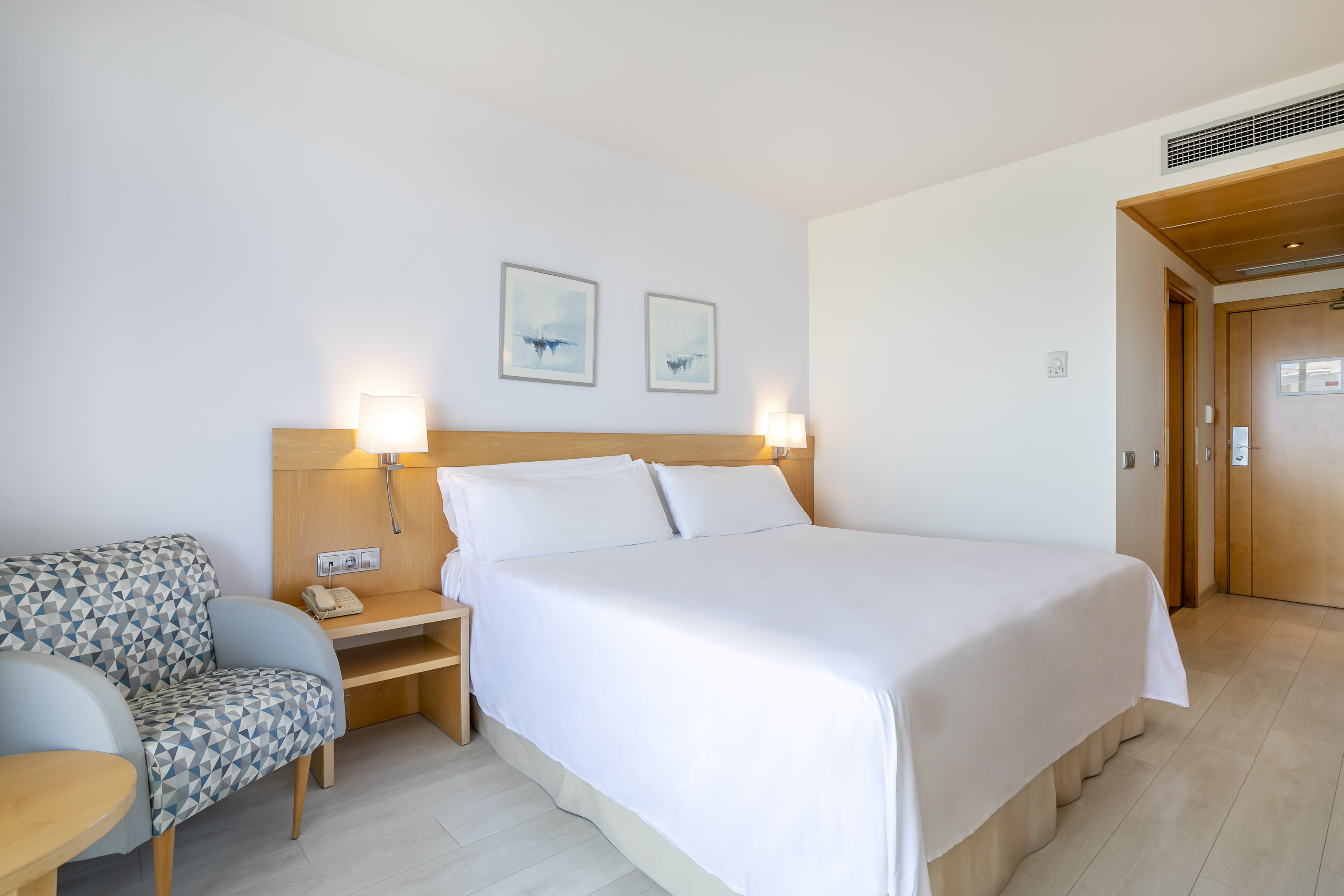 Modern hotel bedroom with king bed, patterned armchair, and wooden floor.