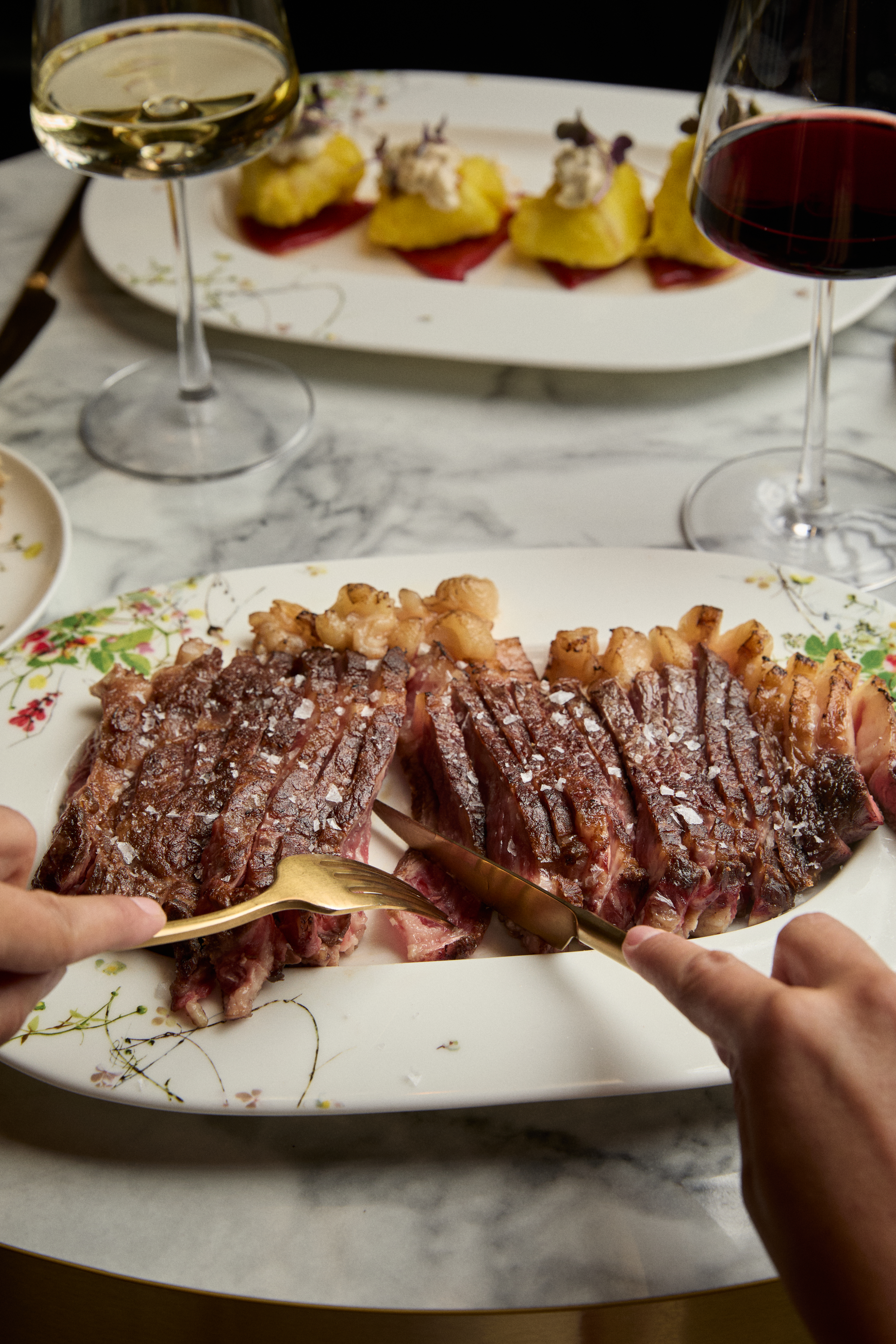 Sliced steak with sea salt, gold cutlery, wine, and small appetizers.