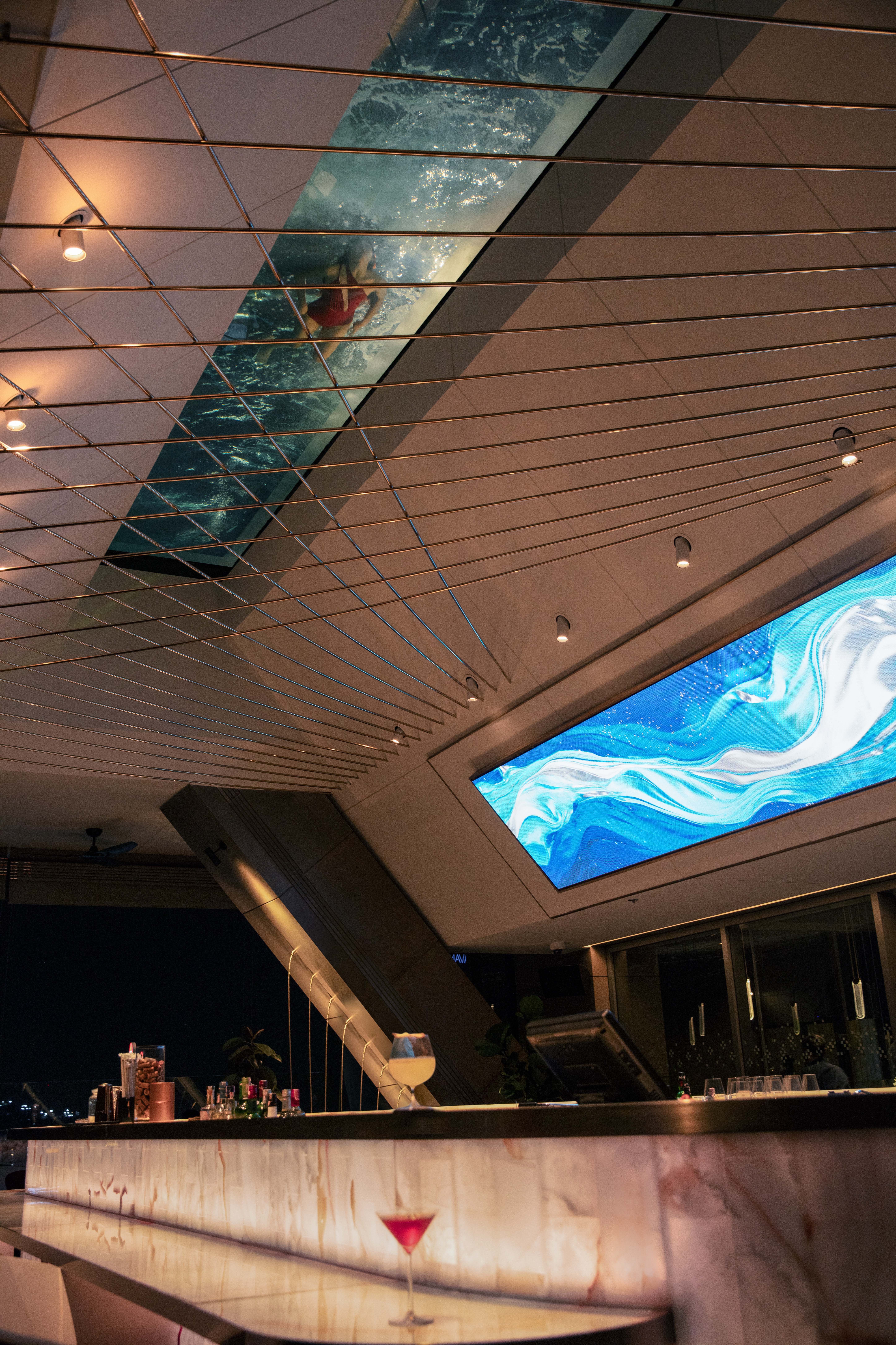 Luxury bar with swimmer in glass-bottom ceiling pool, abstract blue screen.