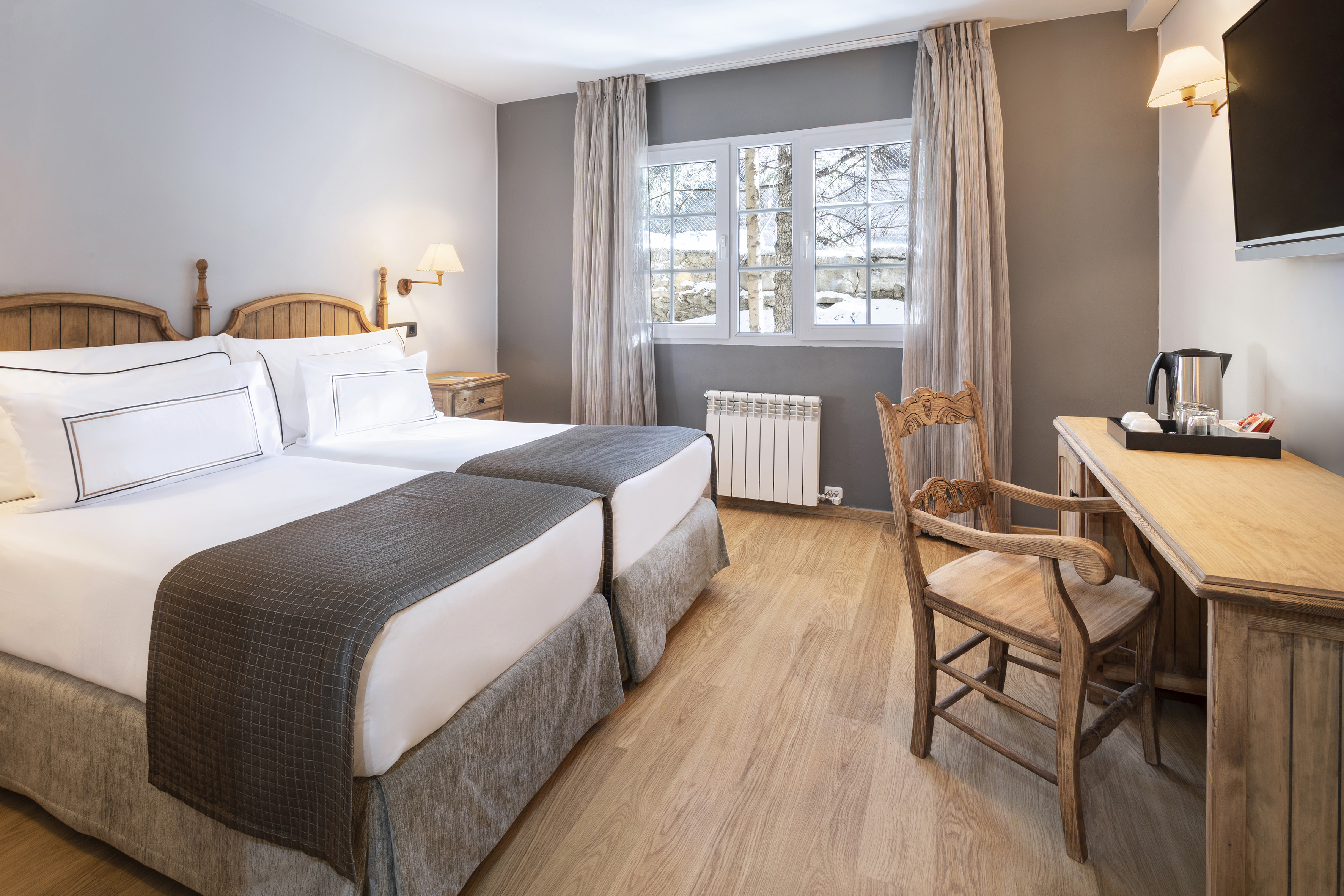 Hotel room with twin beds, wooden decor, and a snowy winter window view.