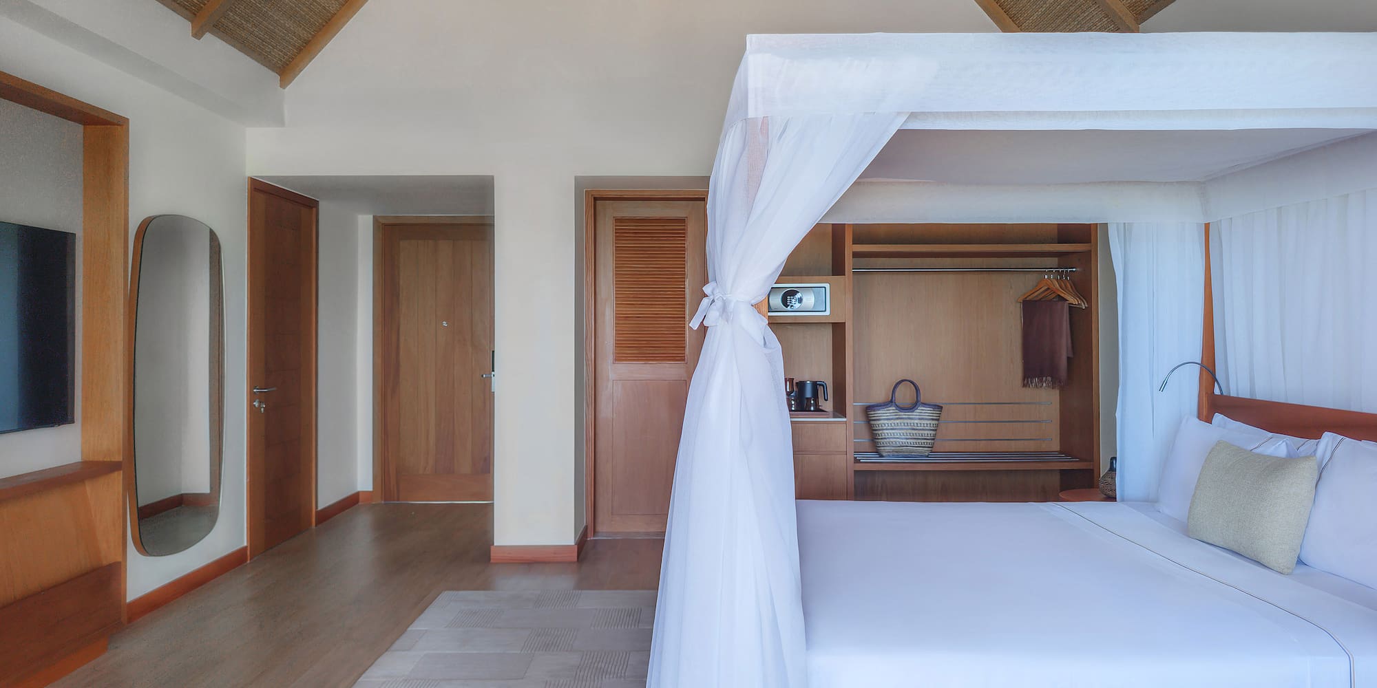 Tropical bedroom with four-poster bed, mosquito net, and vaulted straw ceiling.