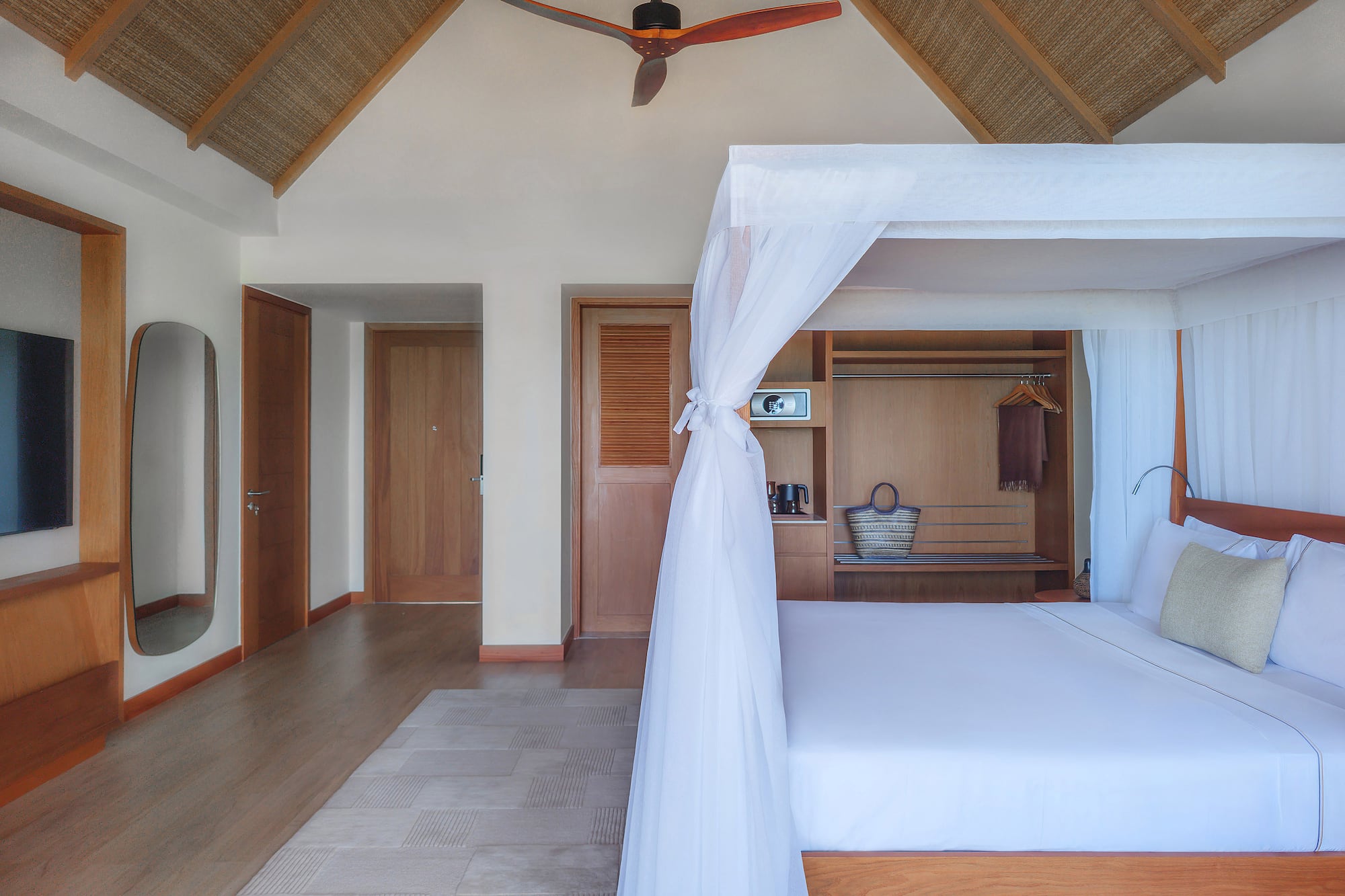 Tropical bedroom with four-poster bed, mosquito net, and vaulted straw ceiling.