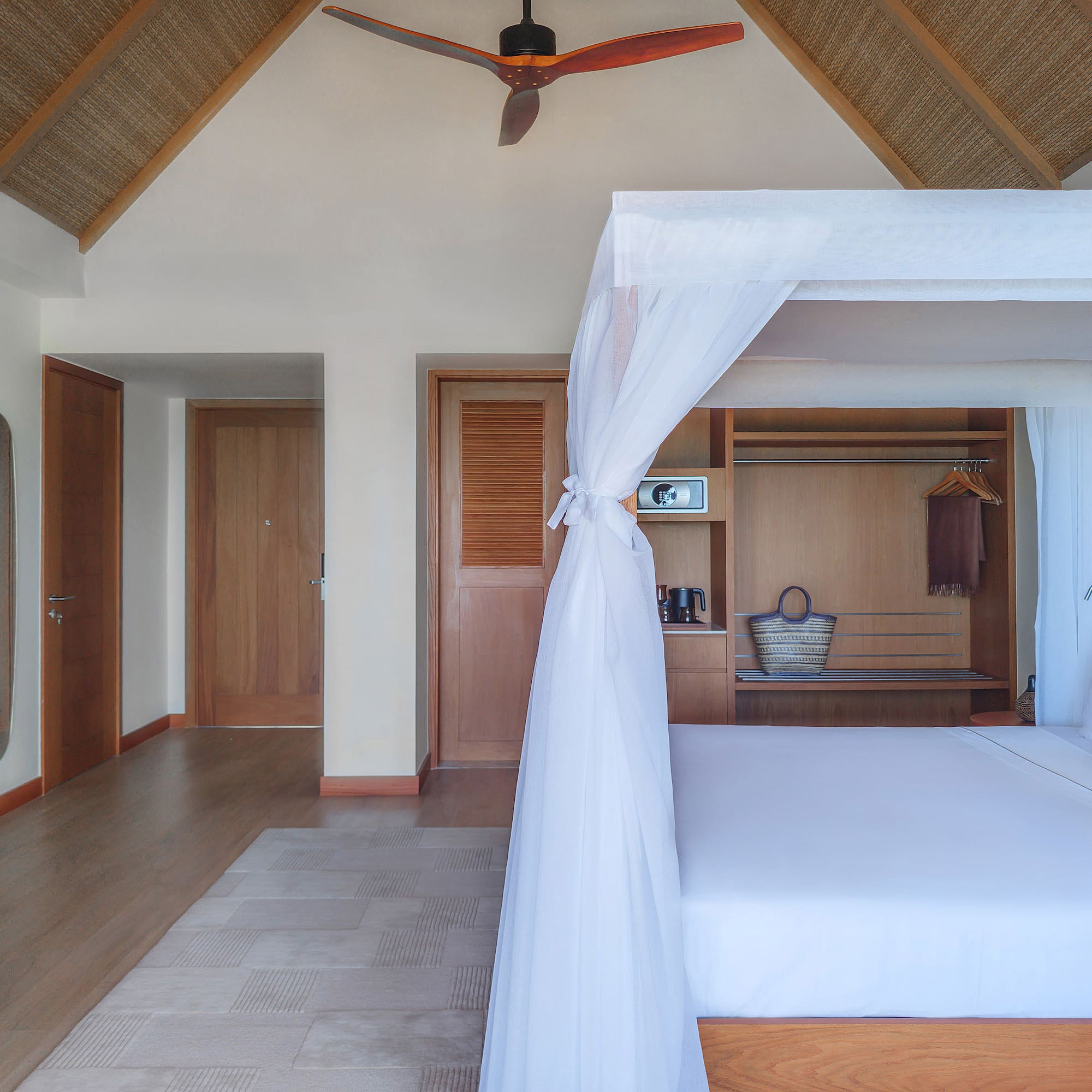 Tropical bedroom with four-poster bed, mosquito net, and vaulted straw ceiling.