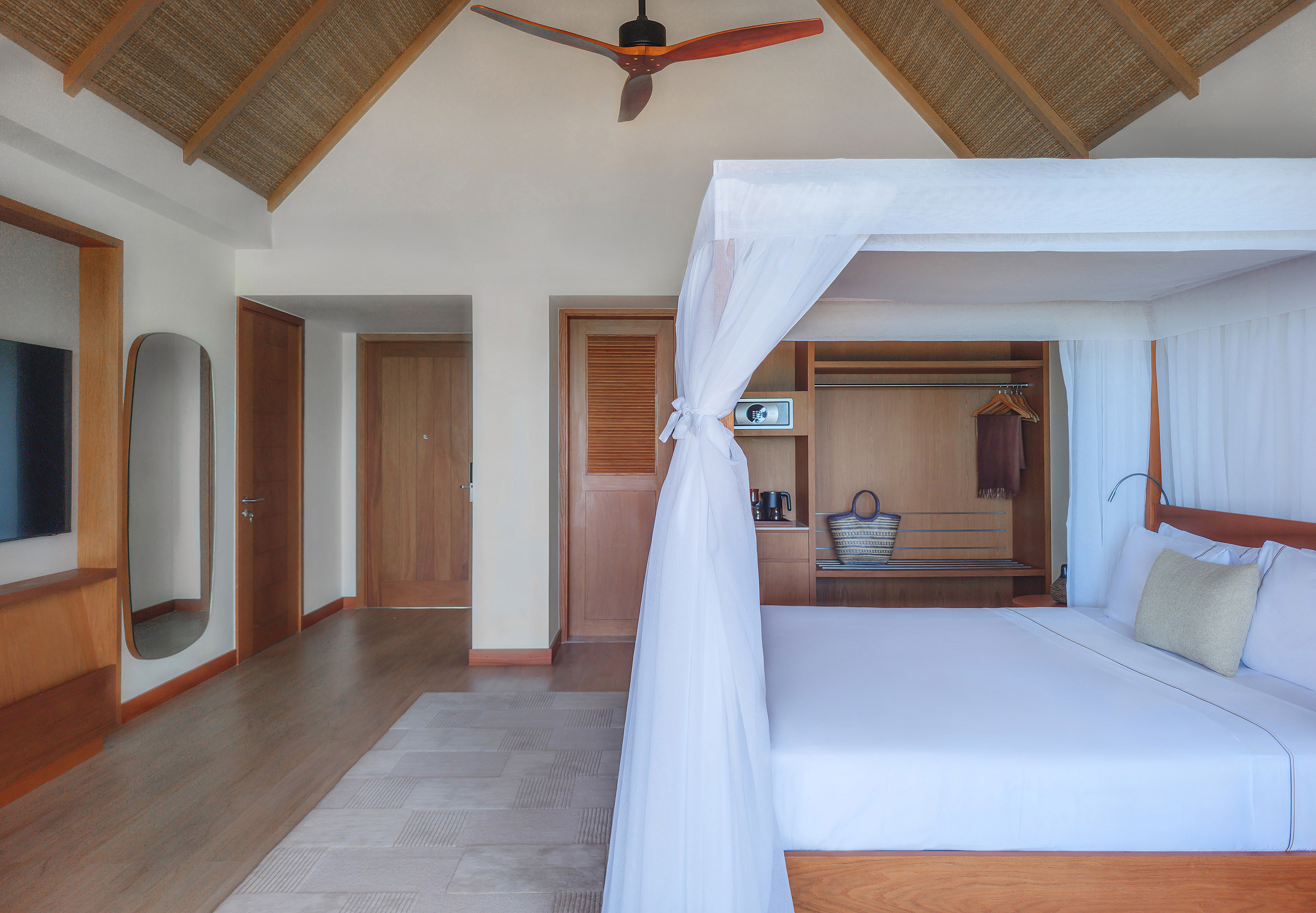 Tropical bedroom with four-poster bed, mosquito net, and vaulted straw ceiling.