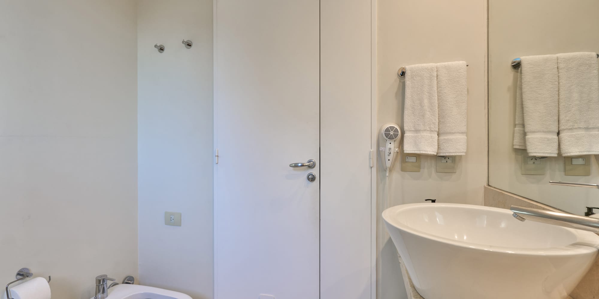 Neutral-toned bathroom with white toilet, bidet, vessel sink, and towels.