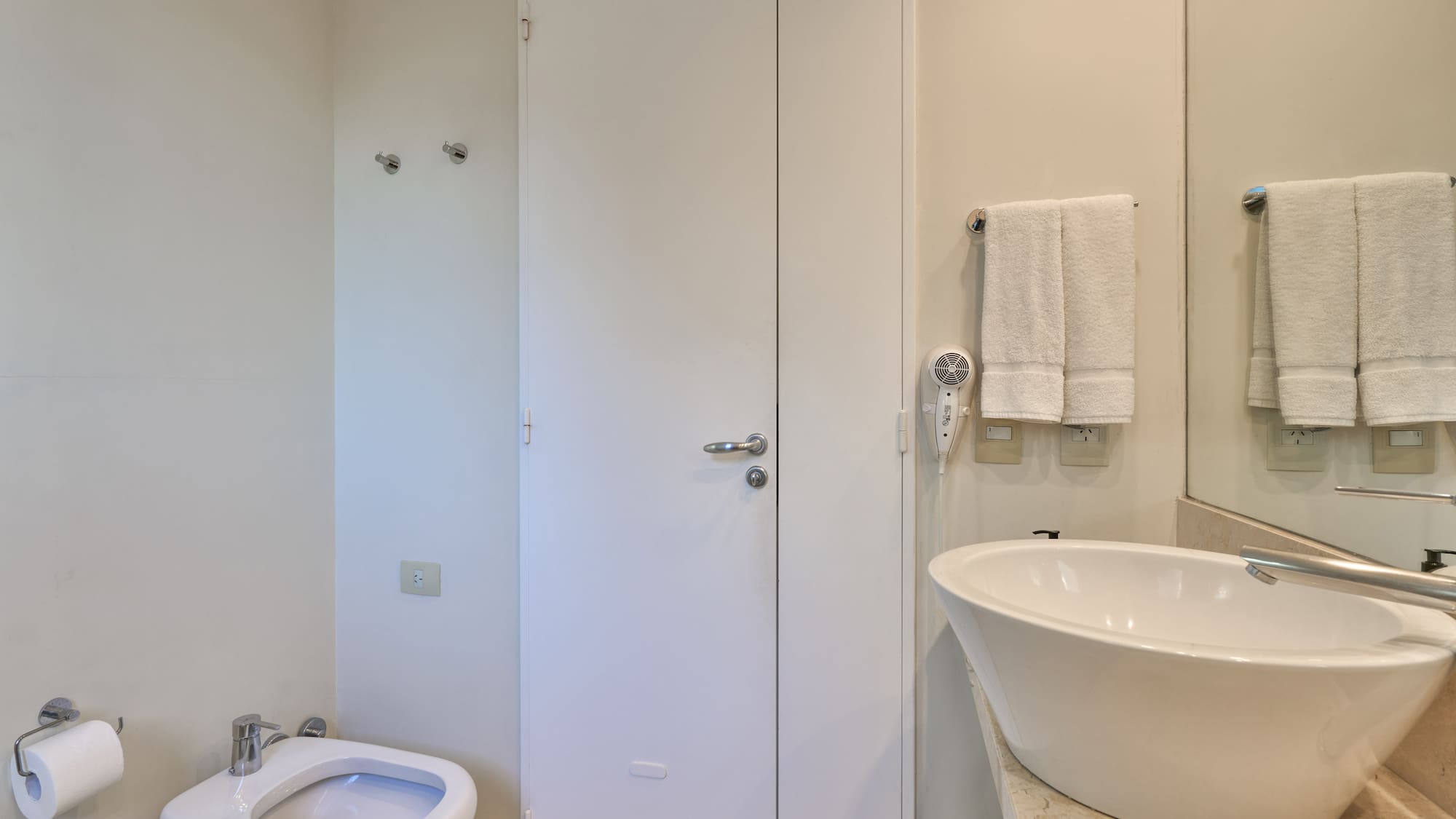 Neutral-toned bathroom with white toilet, bidet, vessel sink, and towels.