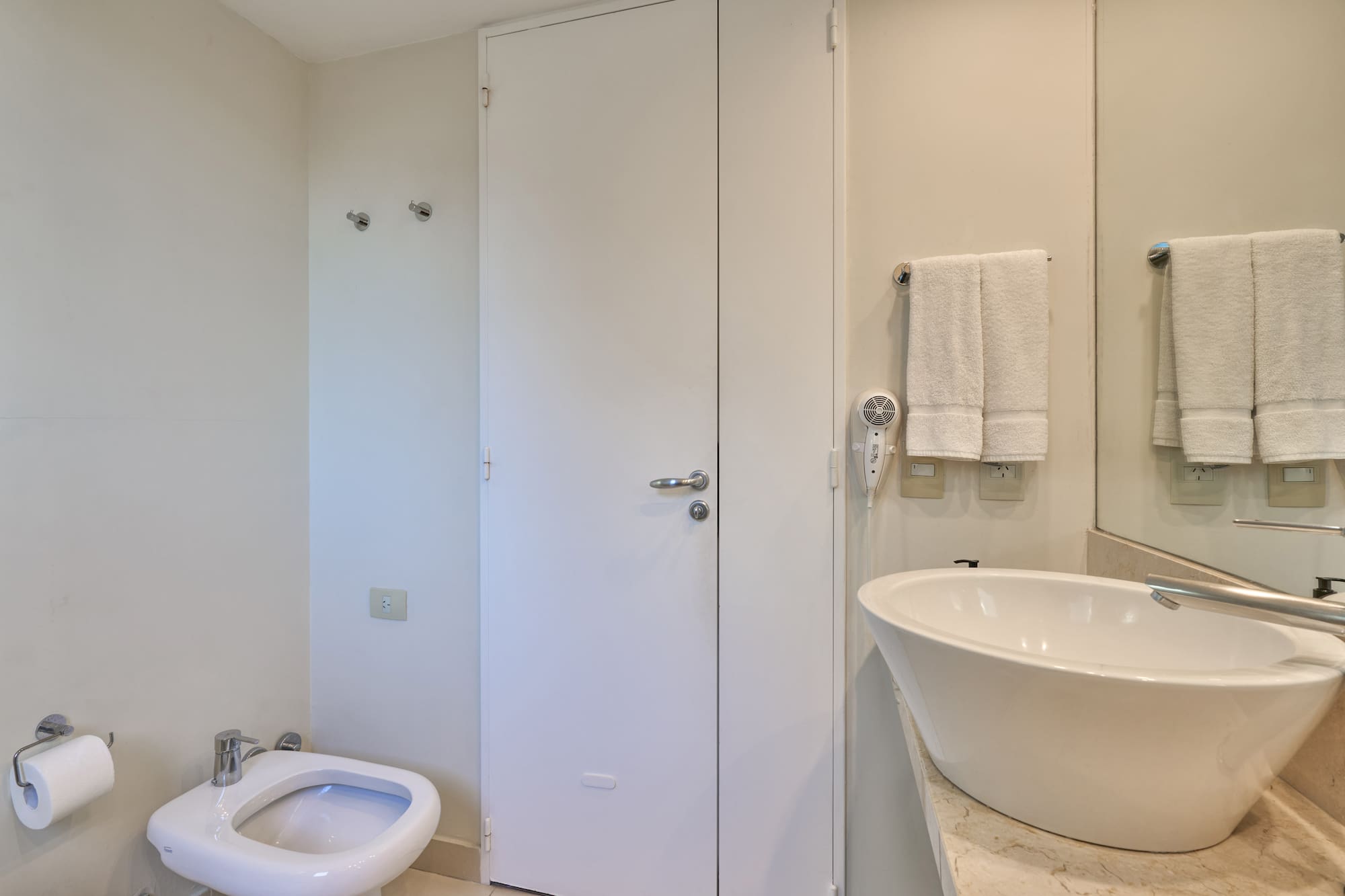 Neutral-toned bathroom with white toilet, bidet, vessel sink, and towels.