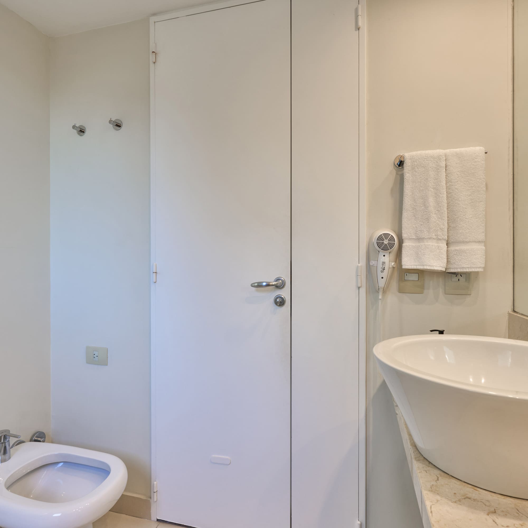 Neutral-toned bathroom with white toilet, bidet, vessel sink, and towels.