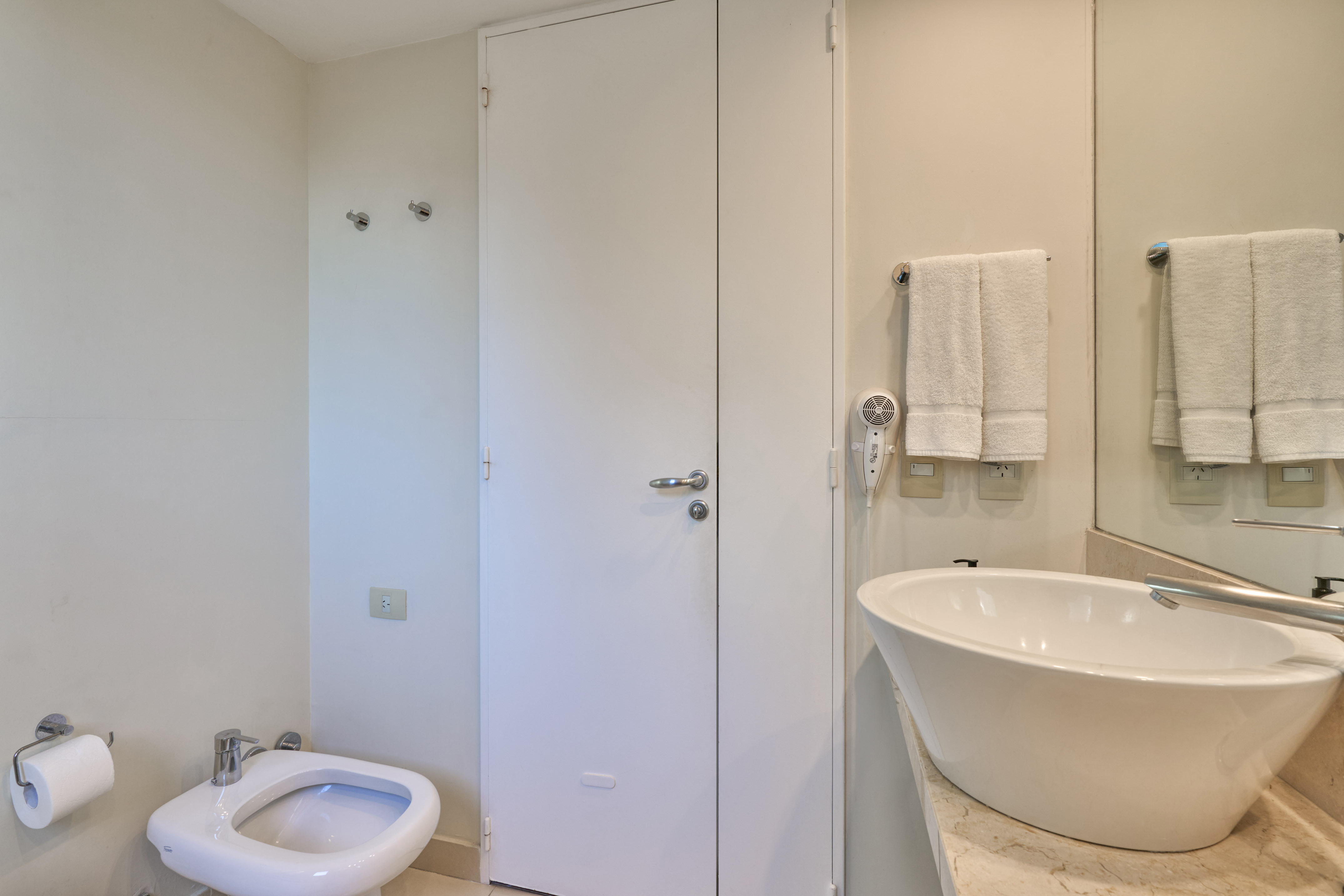 Neutral-toned bathroom with white toilet, bidet, vessel sink, and towels.