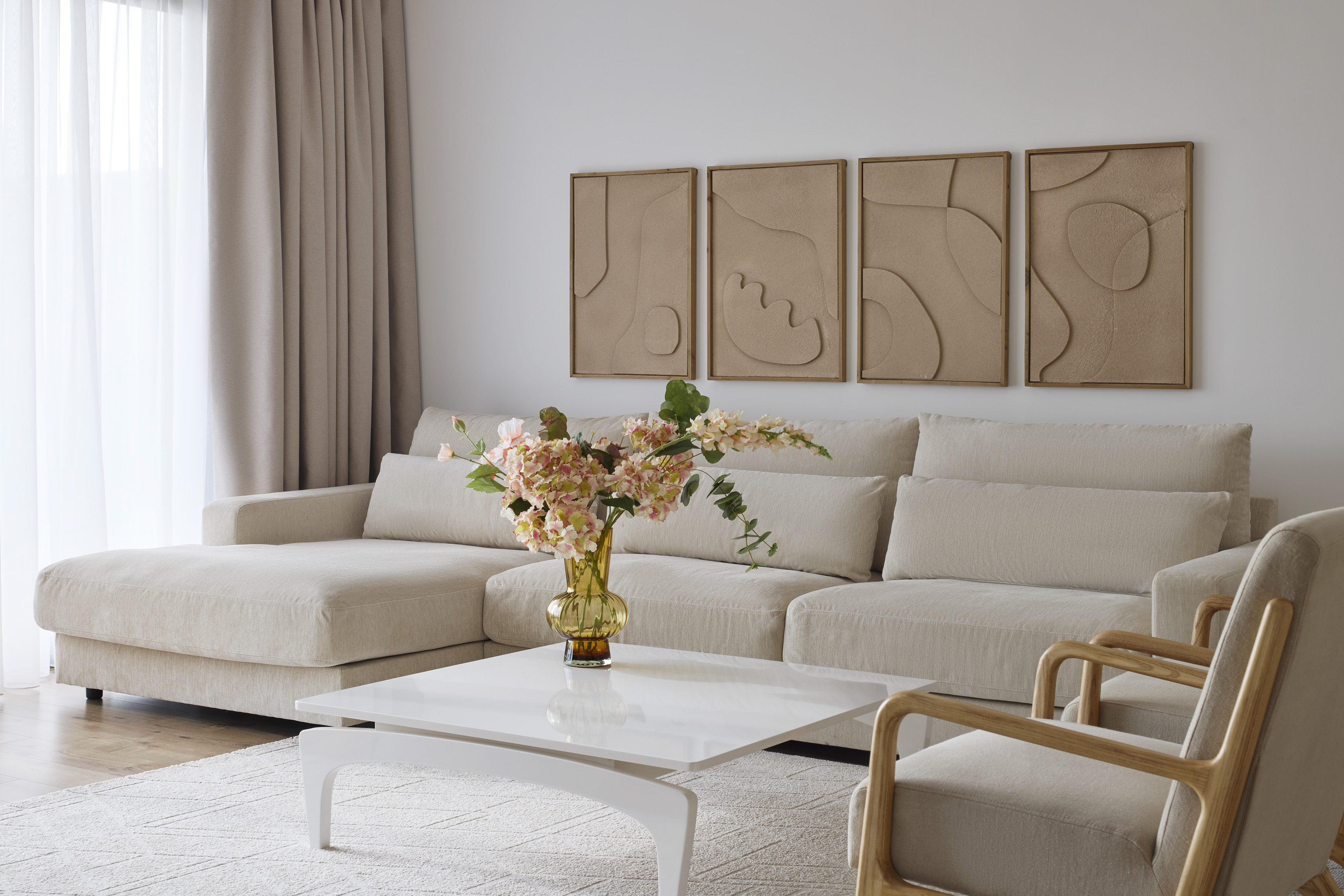 Modern living room with beige sectional sofa, white coffee table, and neutral wall art.