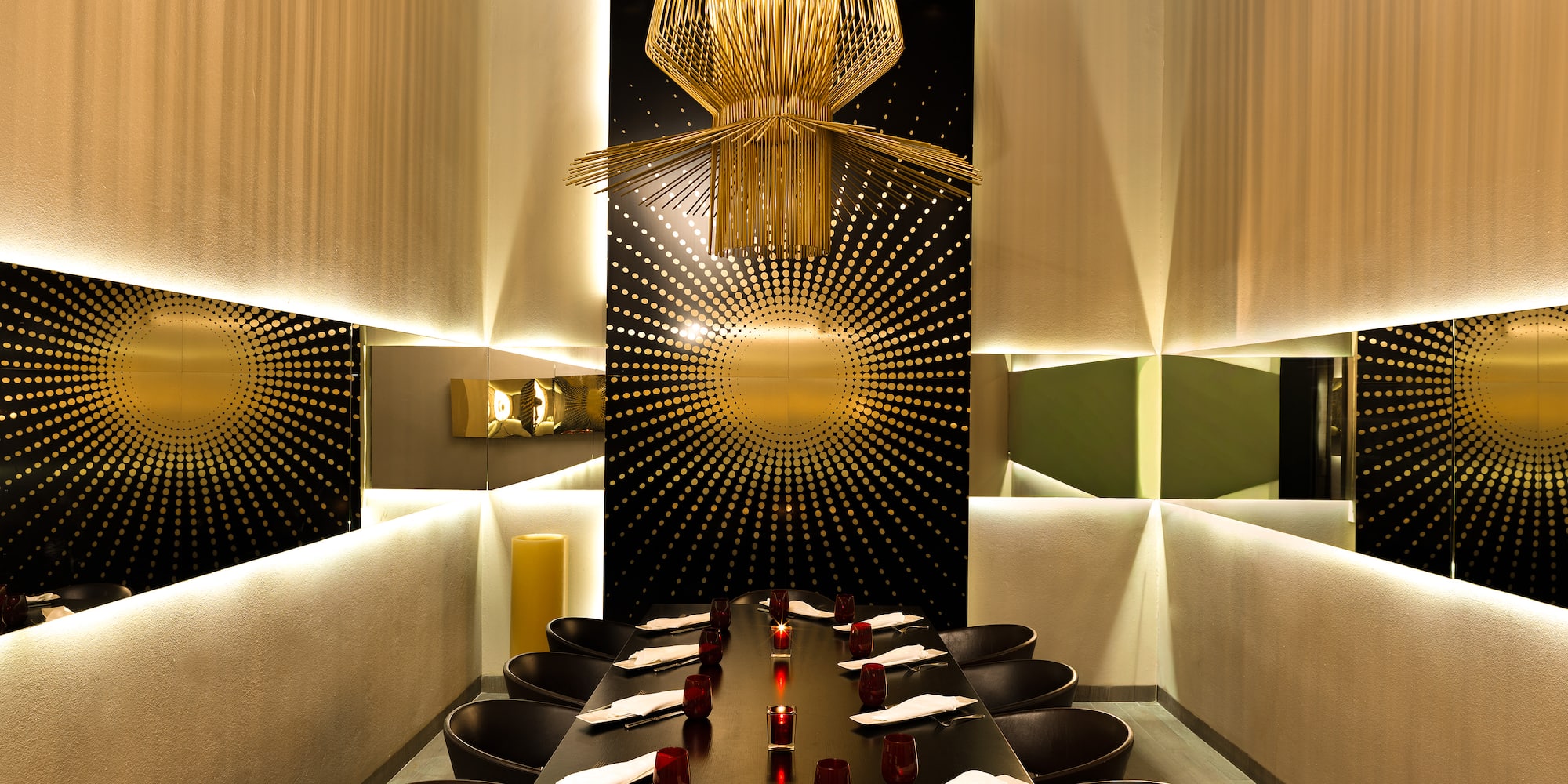 Luxurious private dining room with gold chandelier, sunburst wall, and elegant table.