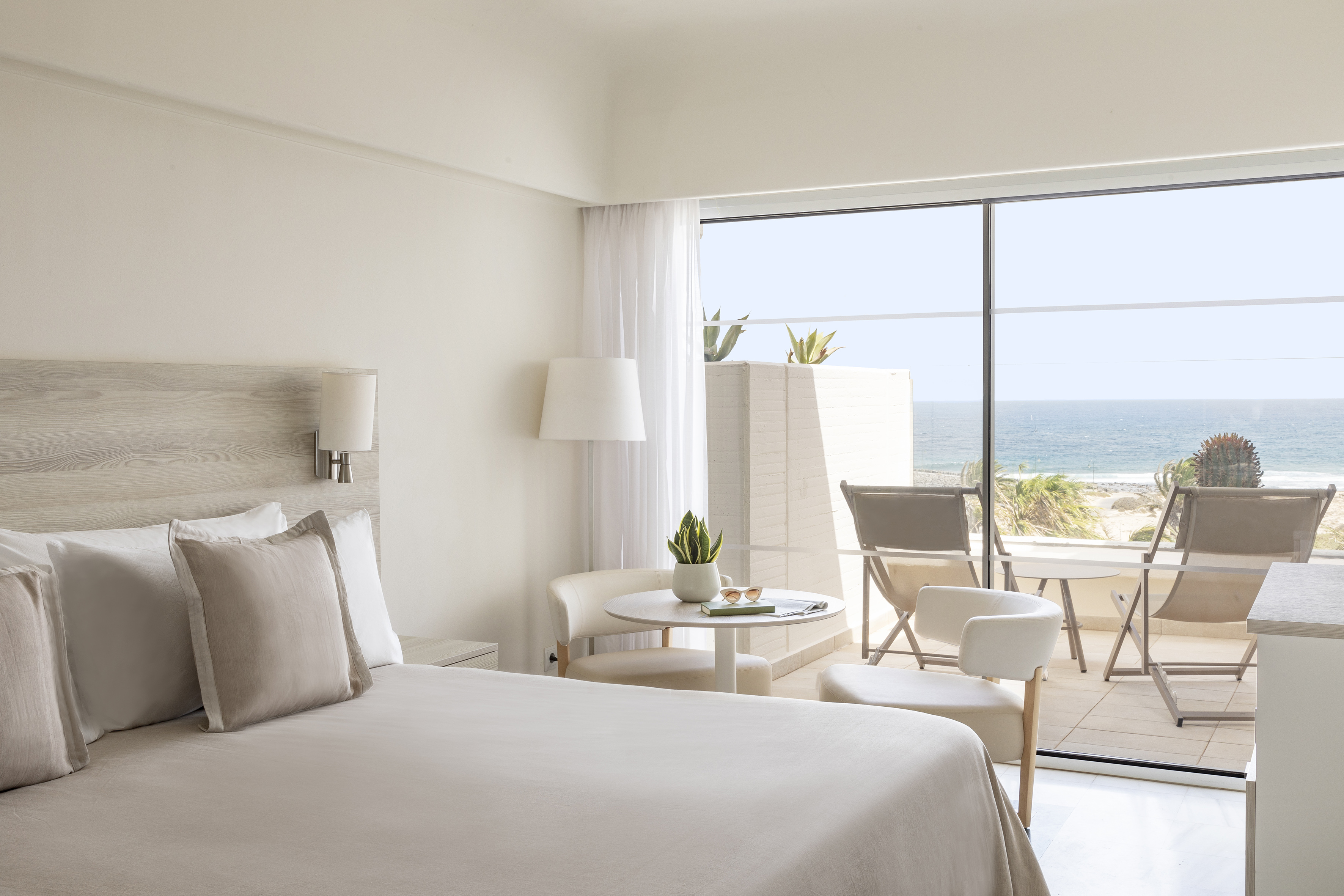 Modern hotel room with beige bed, private balcony, and clear ocean view.