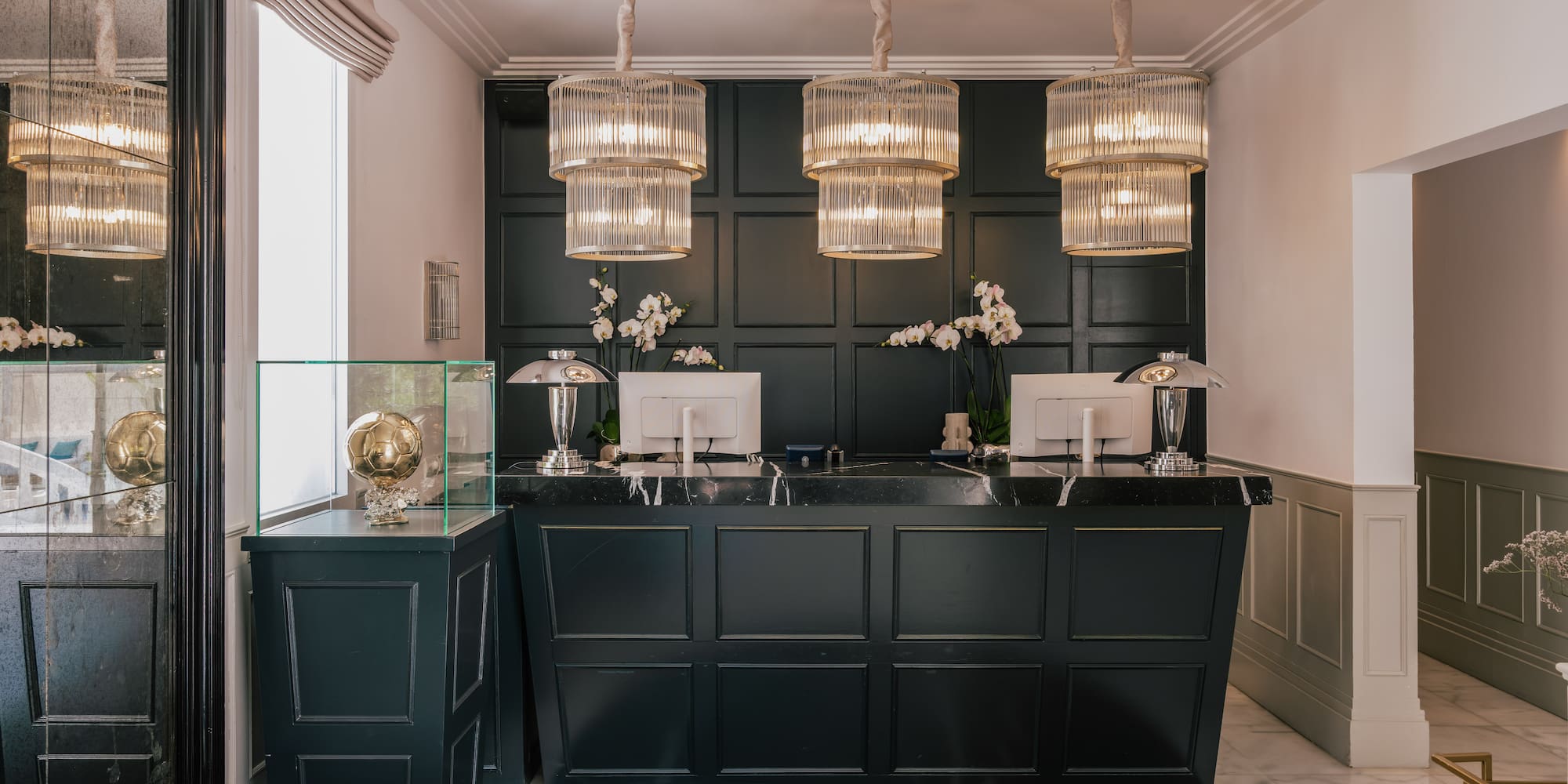 Elegant hotel reception with dark green desk, marble floor, and tiered chandeliers.
