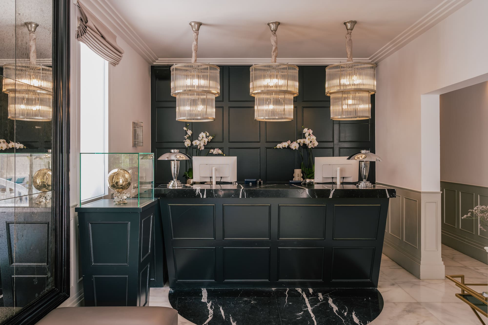 Luxury hotel reception with dark green desk, marble floor, and elegant chandeliers.