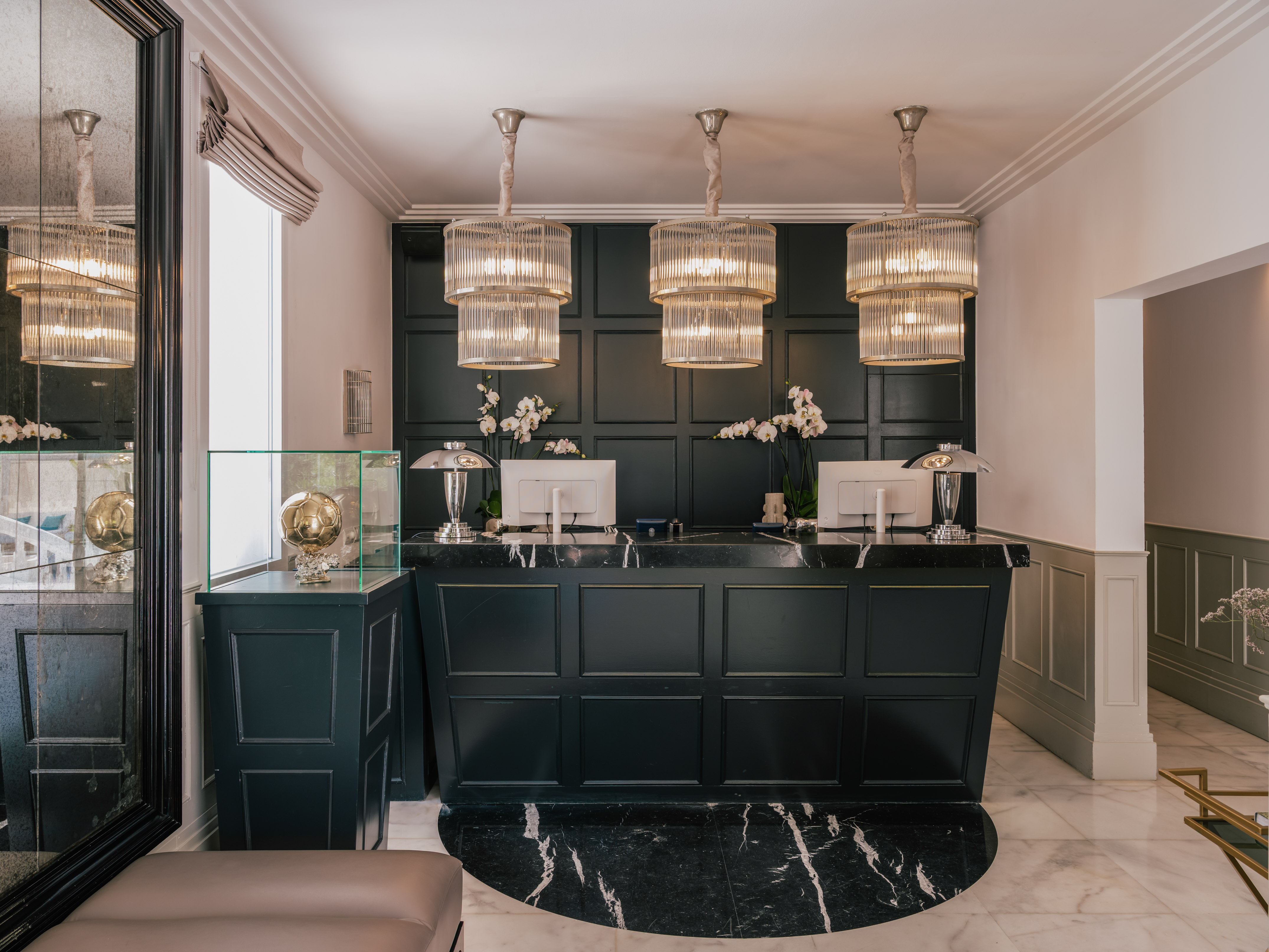 Elegant hotel reception with dark green desk, marble floor, and tiered chandeliers.