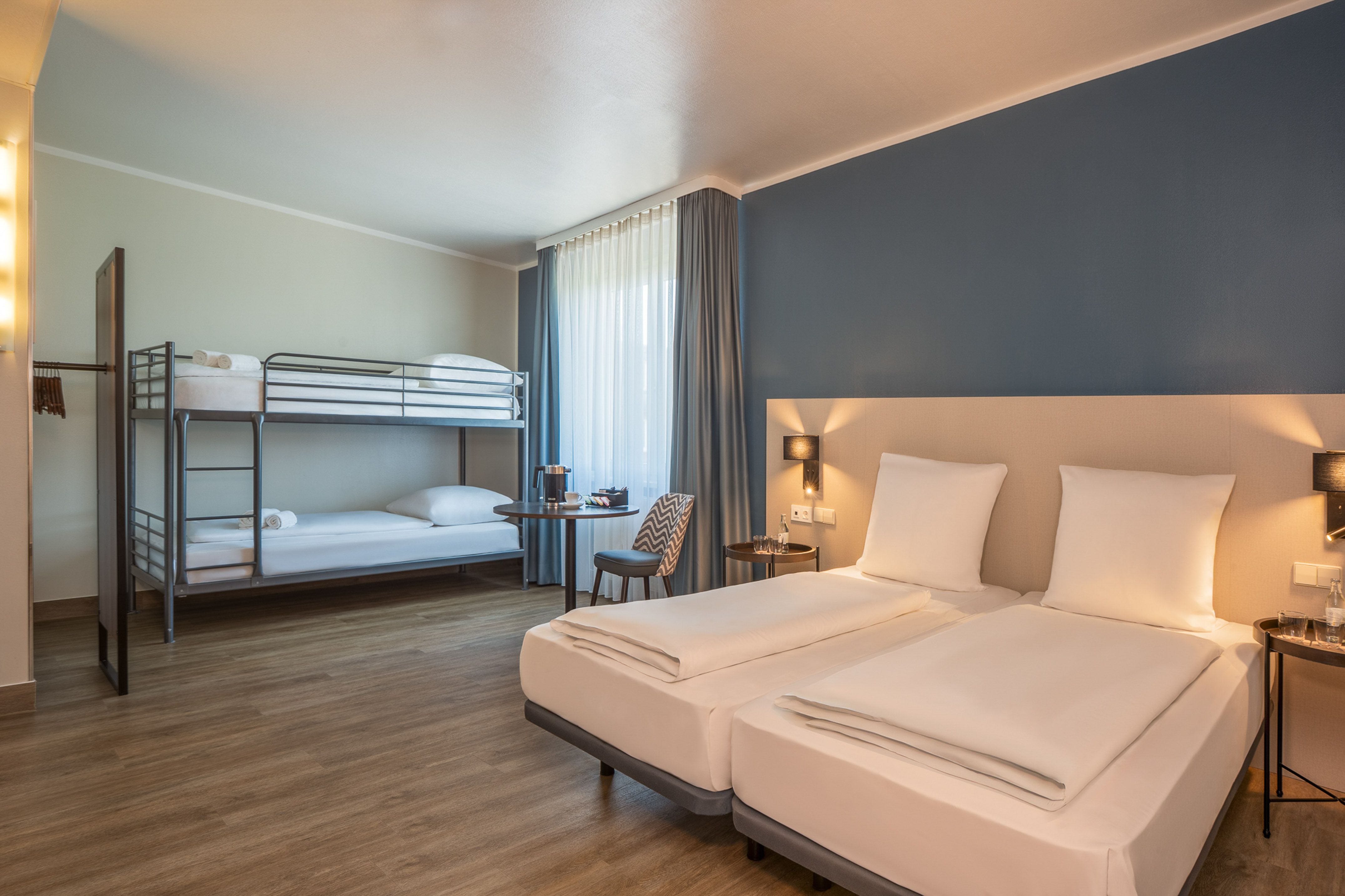 Modern hotel family room with twin beds, bunk beds, and blue accent wall.