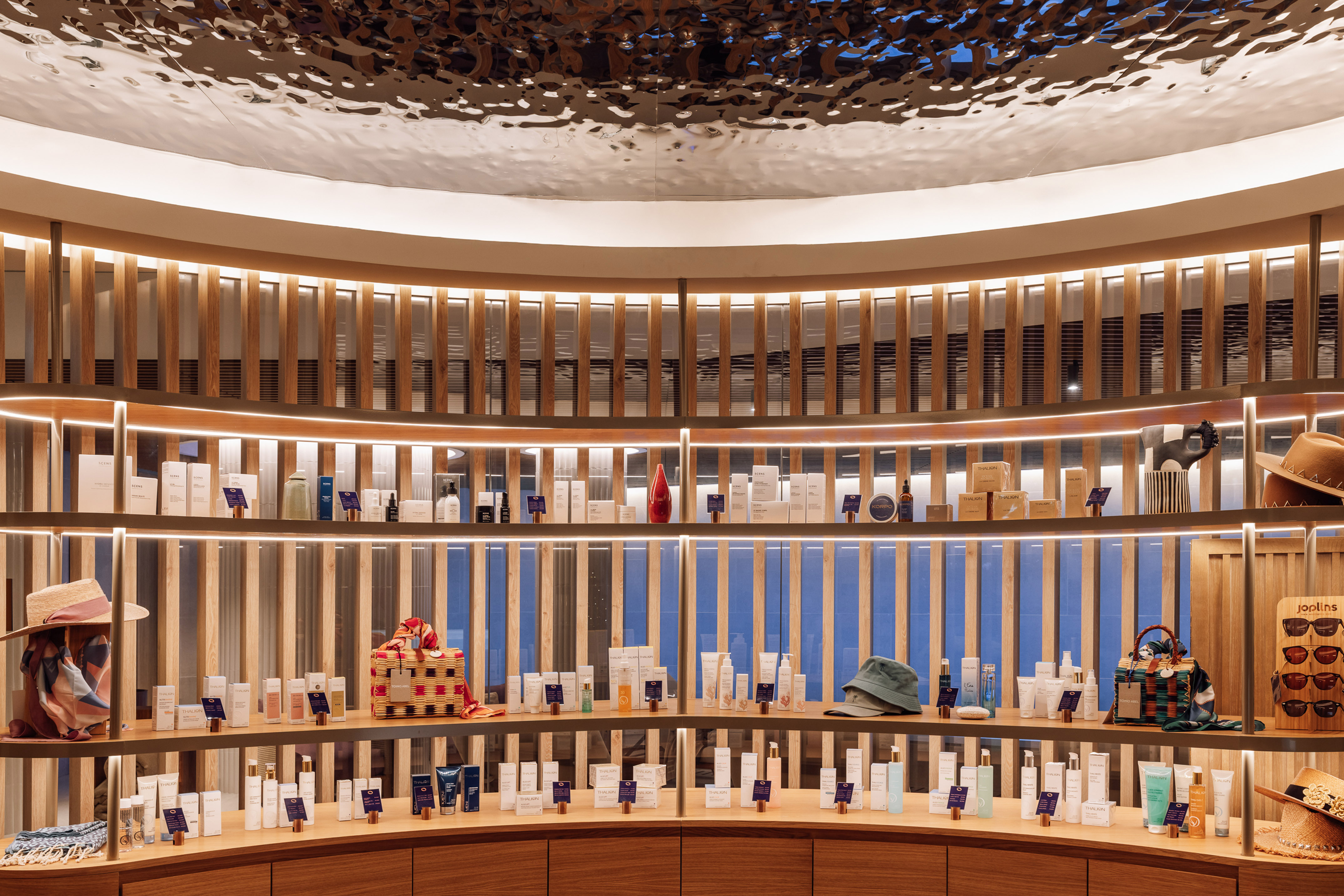 Curved retail display: lit shelves with skincare, beauty products, and hats.
