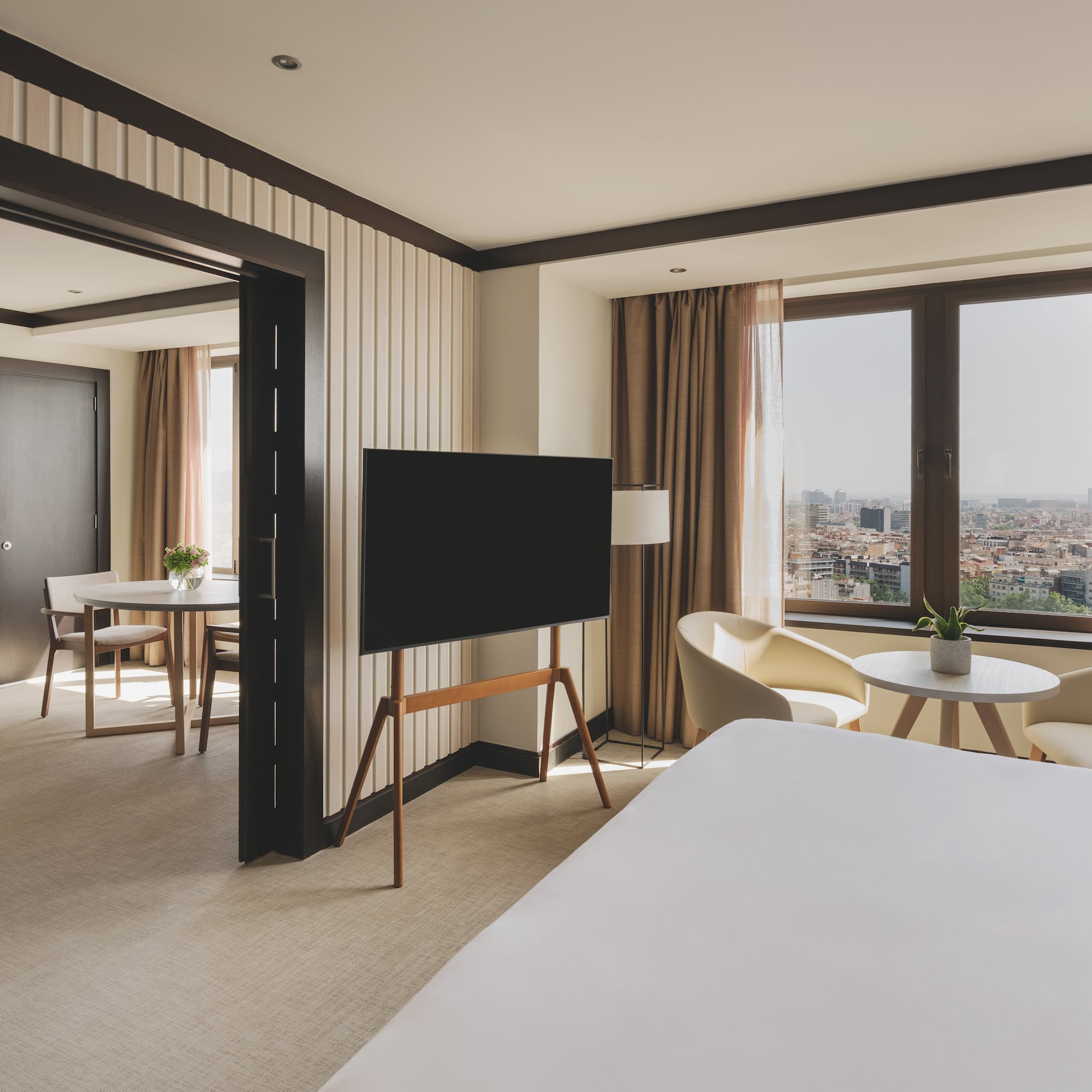 Suite de hotel moderna con dormitorio, TV y vista a la ciudad.