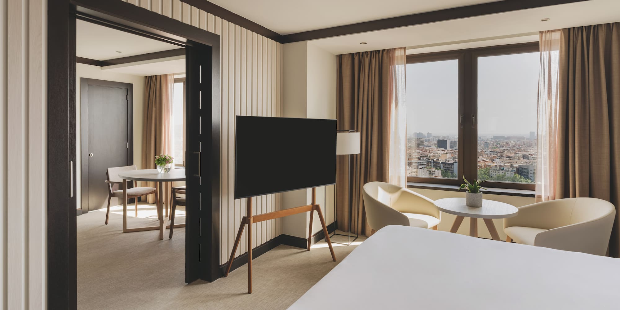 Suite de hotel moderna con dormitorio, TV y vista a la ciudad.