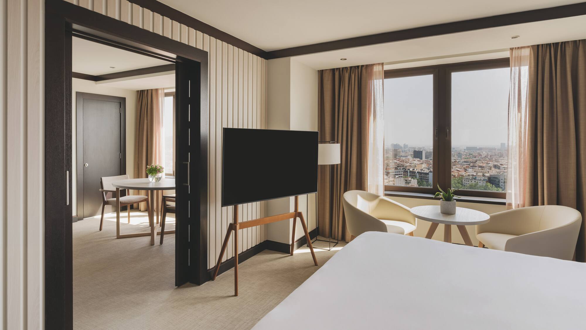 Suite de hotel moderna con dormitorio, TV y vista a la ciudad.